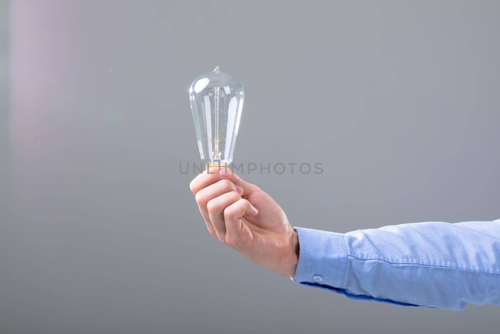 Midsection of caucasian businessman holding light bulb, isolated on grey background. business technology, communication and growth concept.