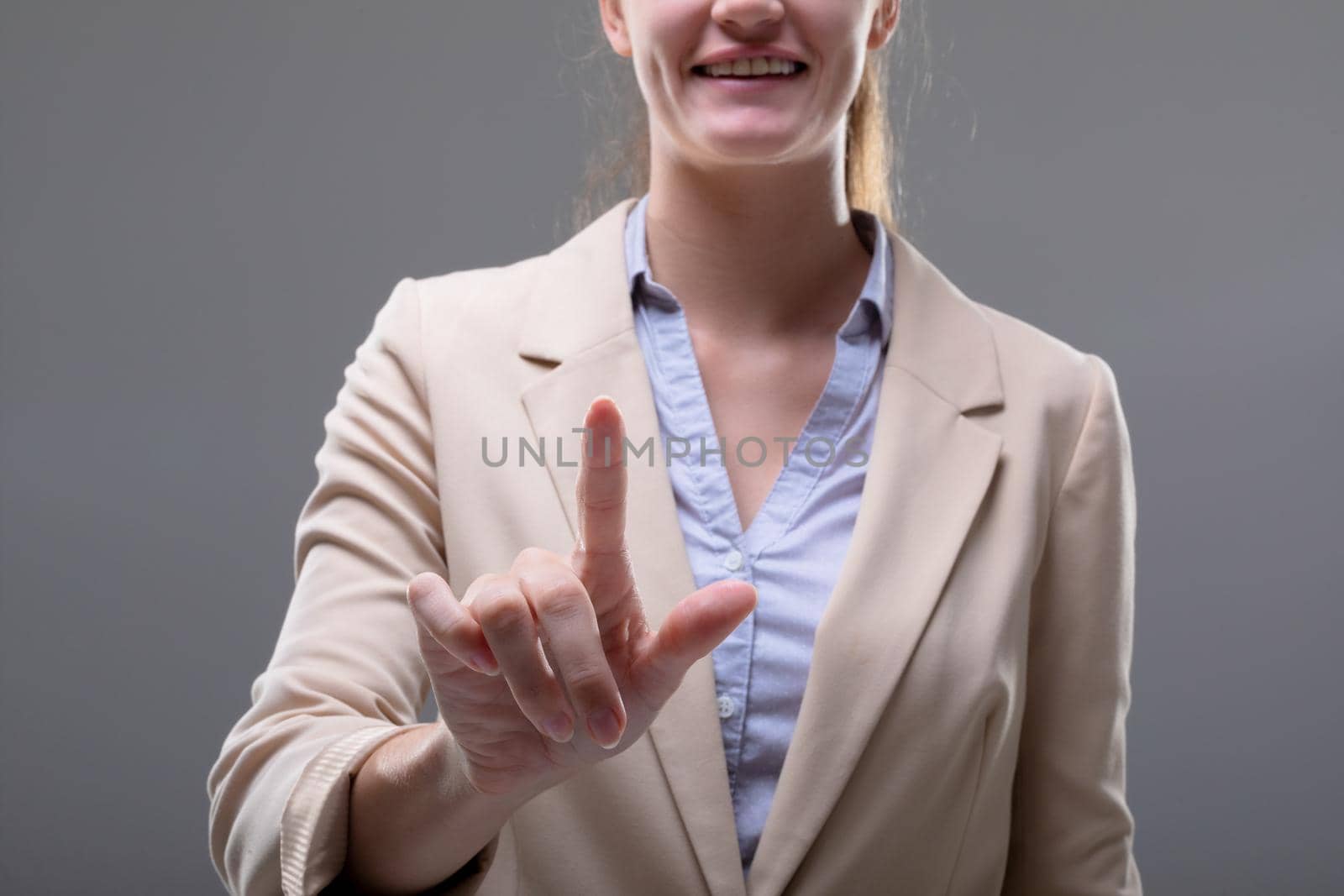 Smiling caucasian businesswoman touching virtual interface on grey background. business, technology, communication and growth concept.