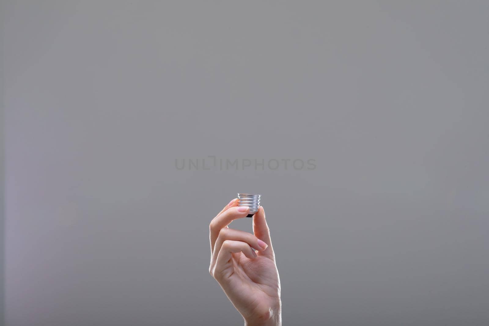 Close up of caucasian businesswoman holding base of light bulb, isolated on grey background. business, technology, communication and growth concept.