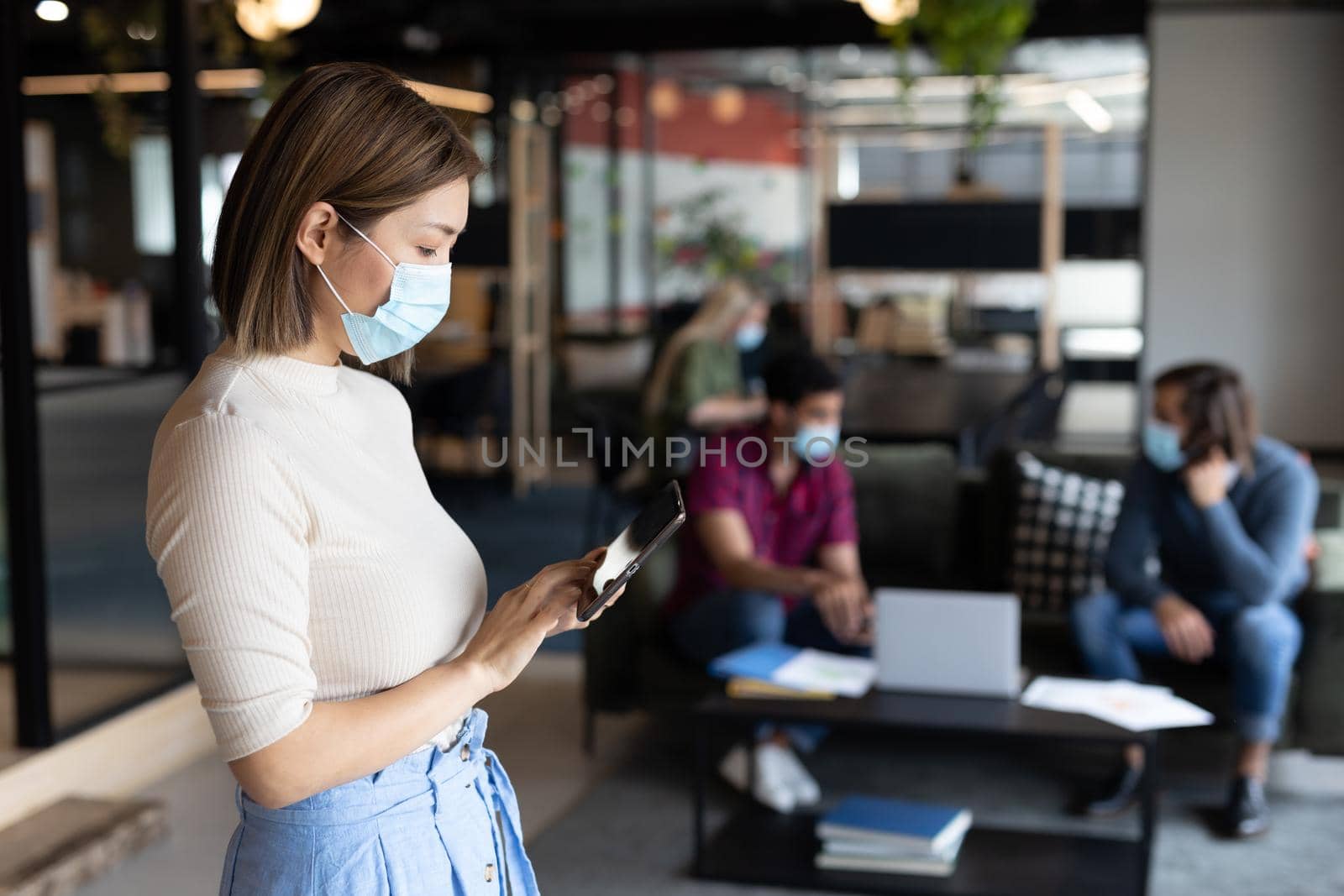 Asian businesswoman wearing face mask using tablet in creative office. social distancing health protection hygiene in workplace during covid 19 pandemic