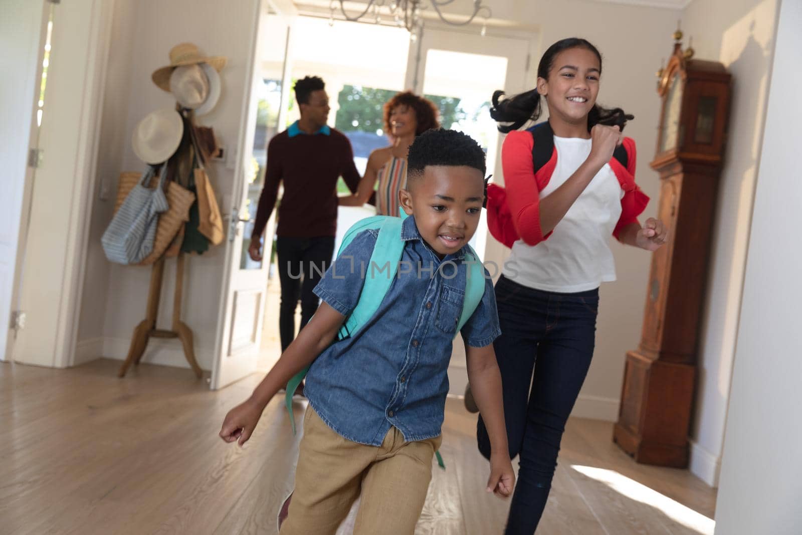 Happy african american couple with son and daughter back from school embracing and smiling at home. family enjoying quality free time together.