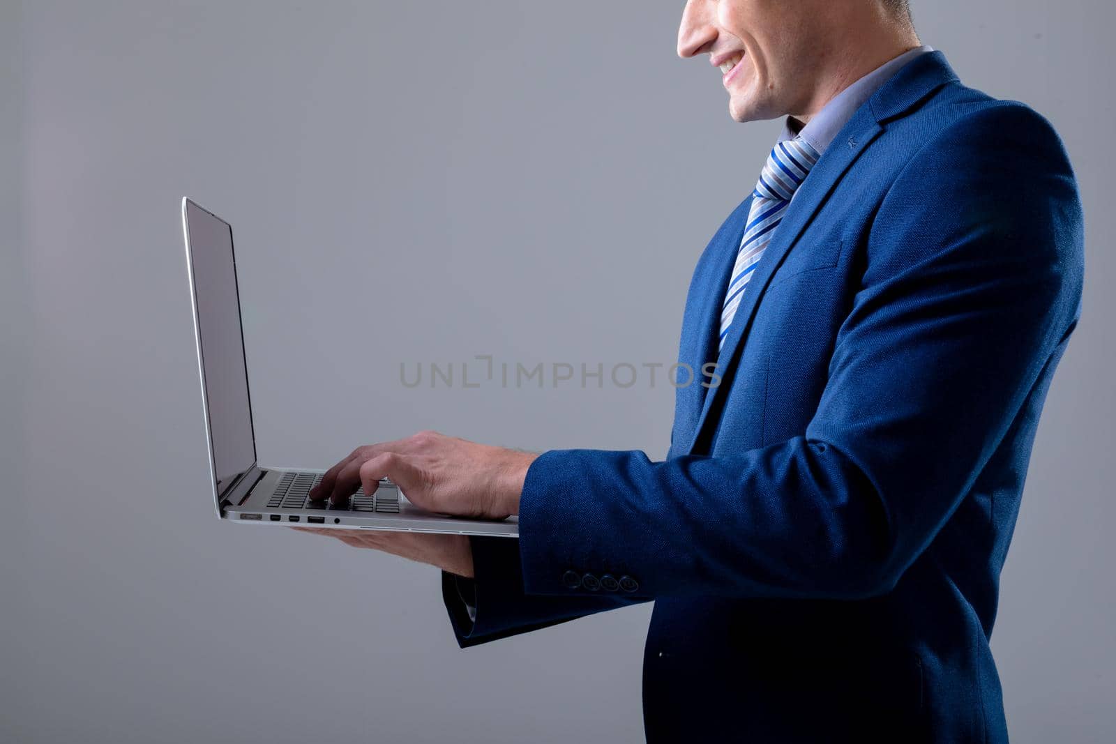 Smiling caucasian businessman using laptop, isolated on grey background. business technology, communication and growth concept digitally generated composite image.