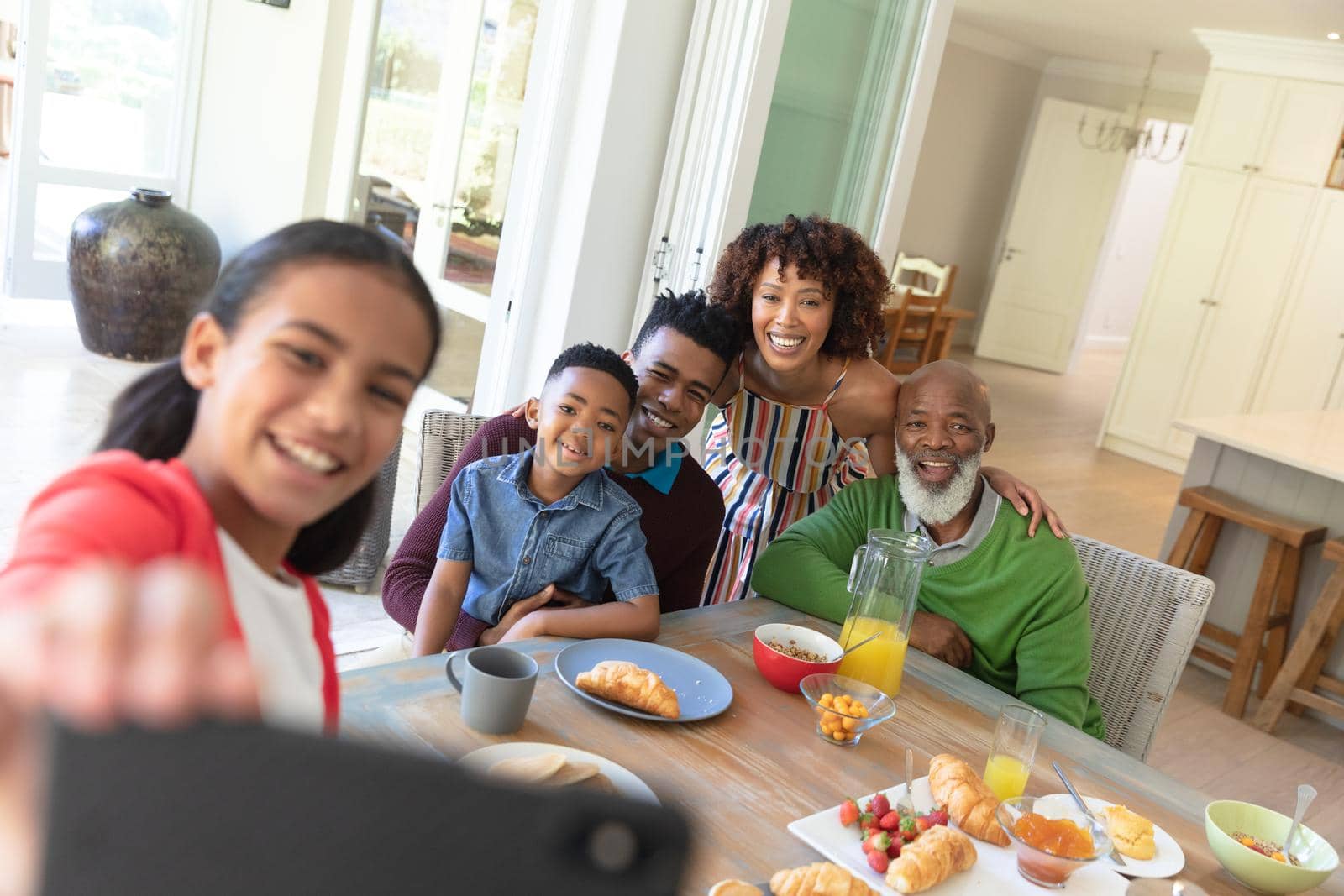 Happy african american family sitting at breakfast table taking selfie with smartphone and smiling. family enjoying quality free time together.