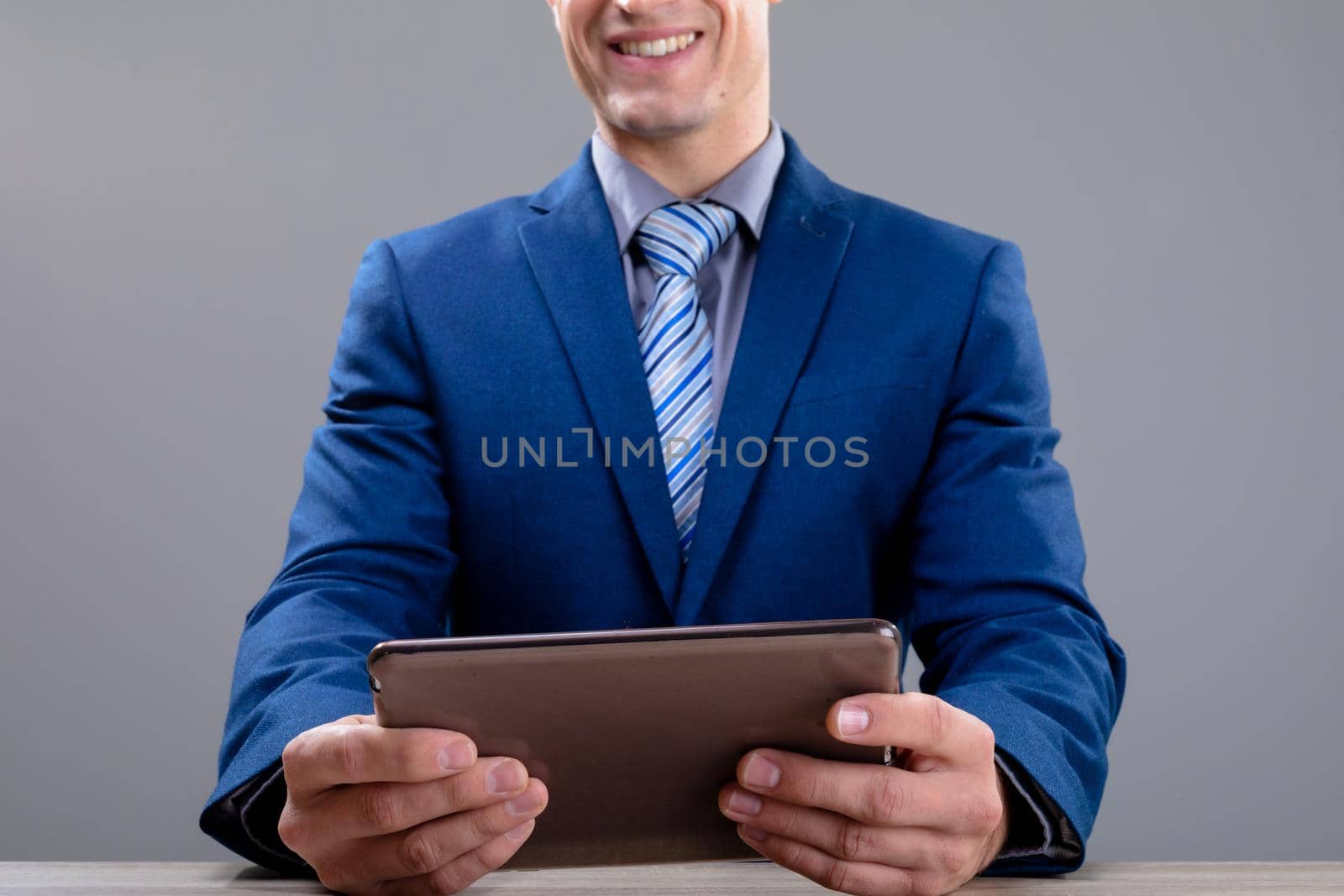 Smiling caucasian businessman using tablet, isolated on grey background. business technology, communication and growth concept.