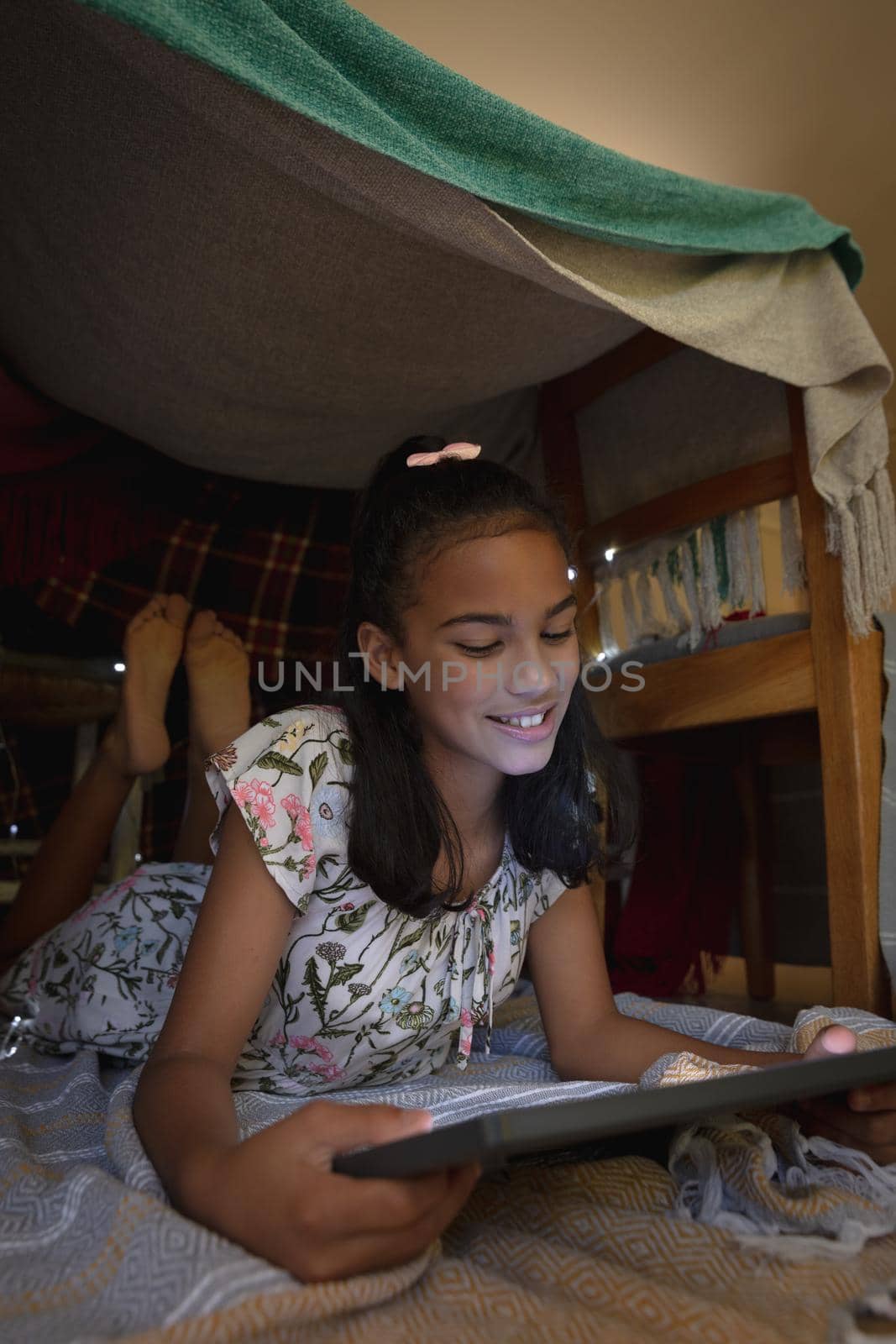 Happy african american girl at home, lying in blanket fort and using tablet by Wavebreakmedia