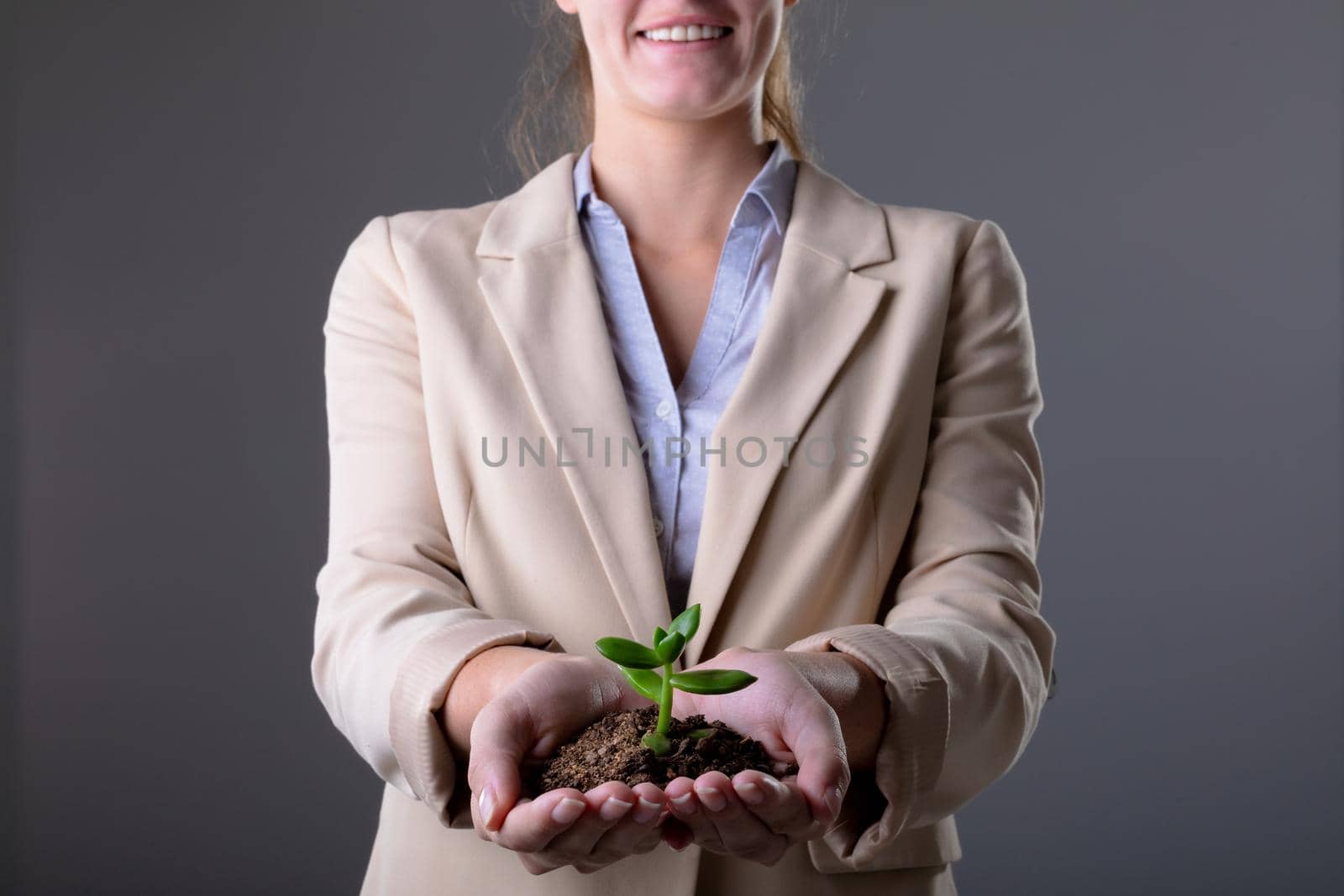 Smiling caucasian businessman holding plant seedling, isolated on grey background. business, technology, communication and growth concept.