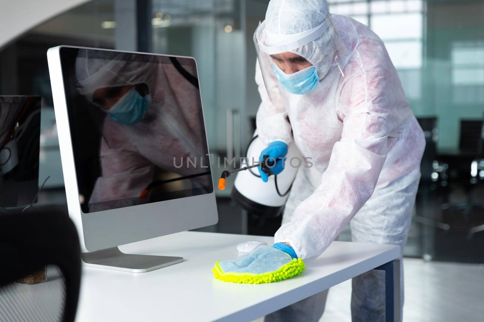 Cleaner wearing protective face mask and overalls disinfecting office and furniture. hygiene in workplace during coronavirus covid 19 pandemic.
