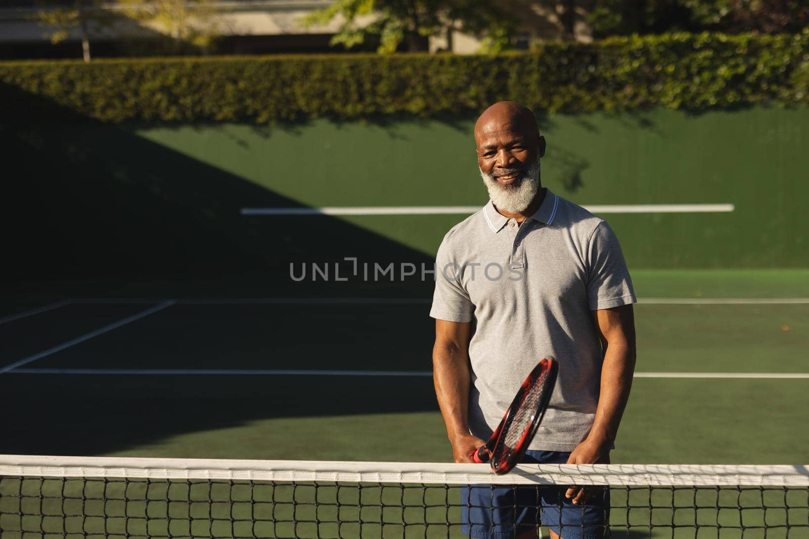 Portrait of smiling senior african american man holding tennis racket on tennis court. retirement and active senior lifestyle concept.