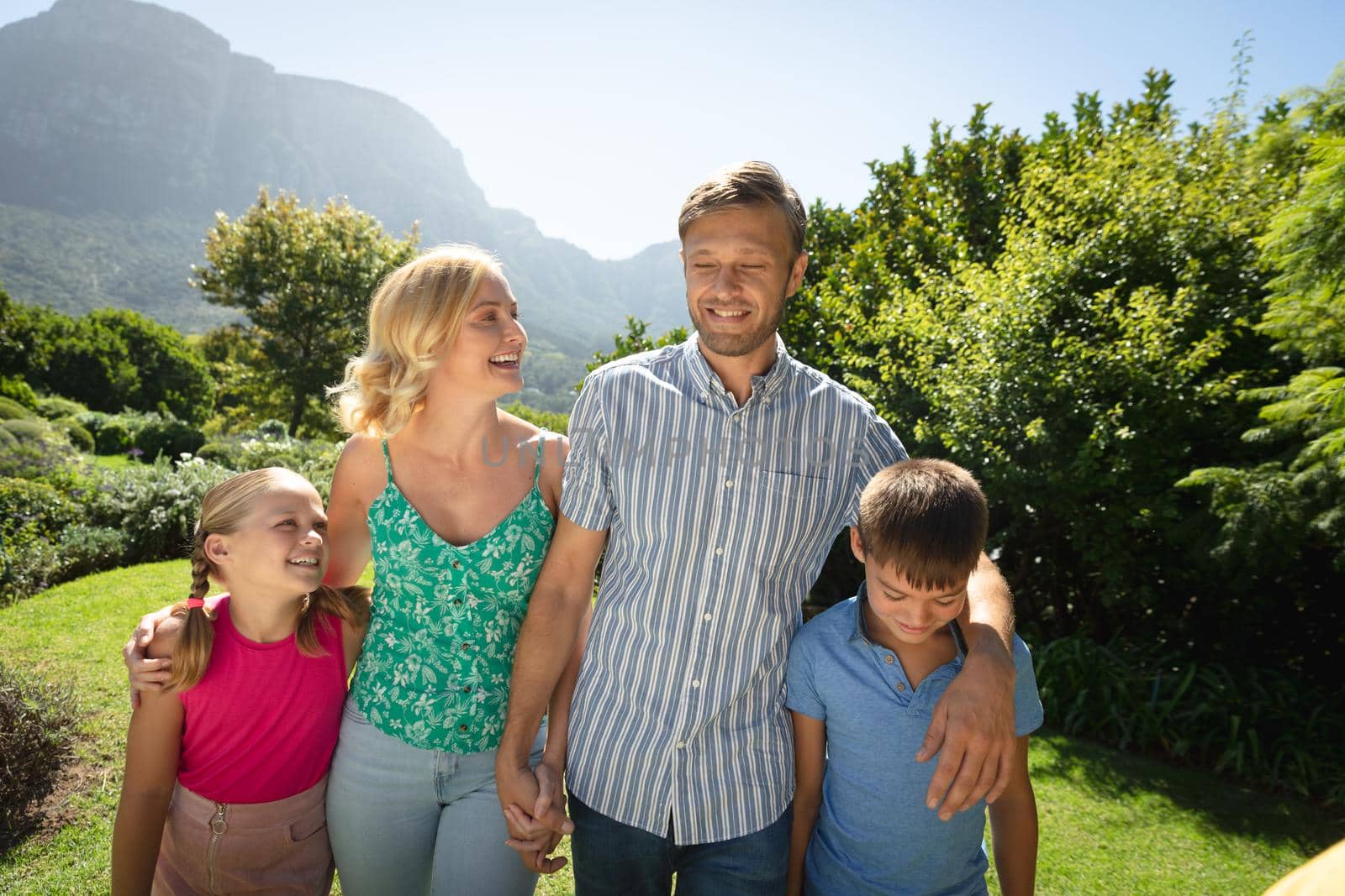 Happy caucasian couple with daughter and son outdoors, walking in sunny garden. family quality time, leisure time concept. family enjoying quality free time together.