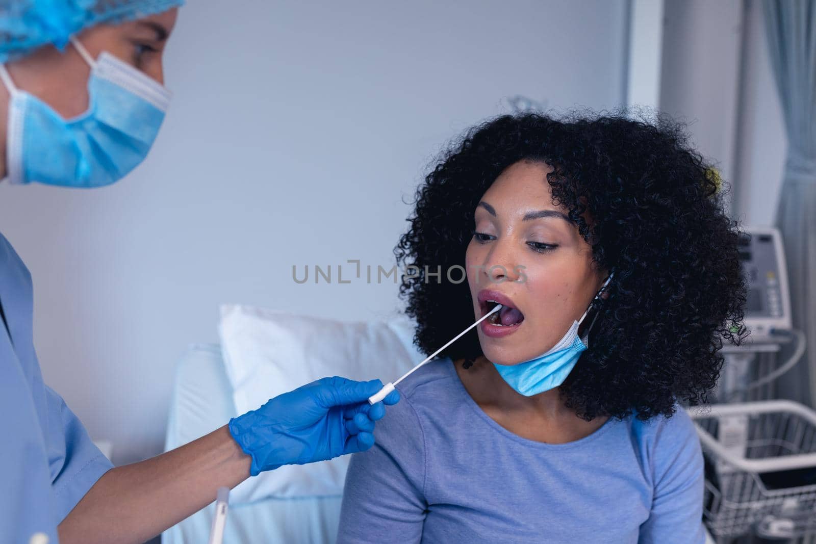 African american female patient with mouth open tested with swab test by female doctor in face mask. medical professional at work during coronavirus covid 19 pandemic.