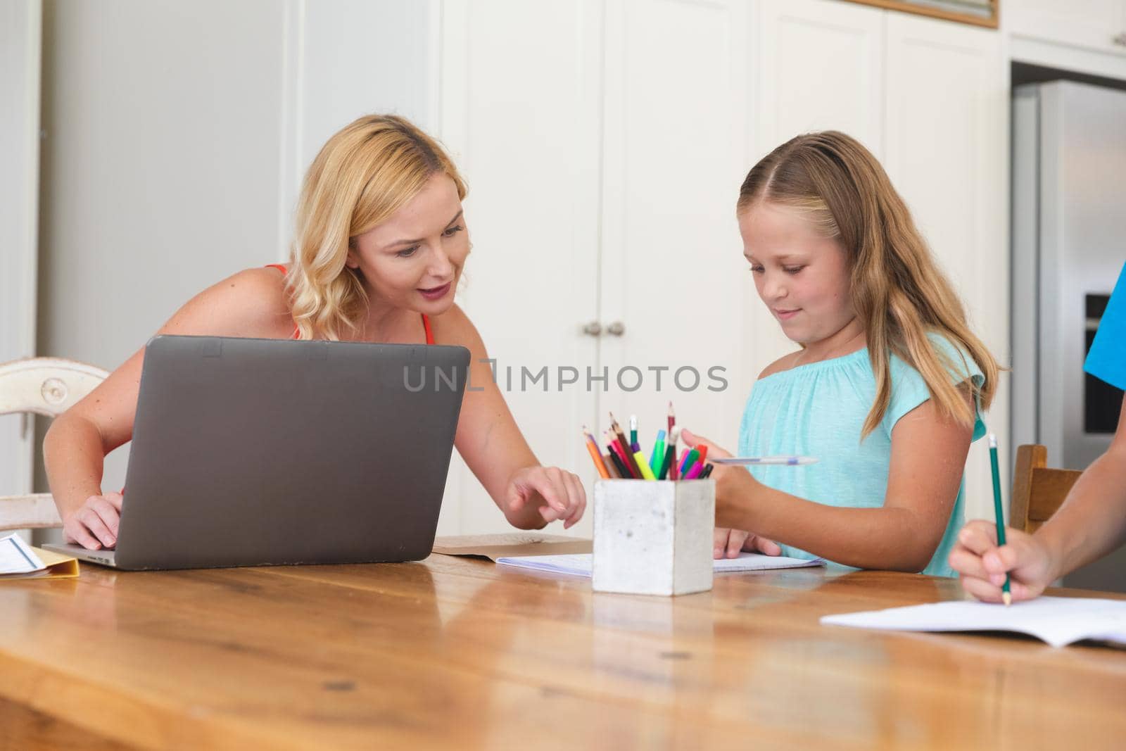 Caucasian mother using laptop and doing homework with her daughter smiling at home by Wavebreakmedia