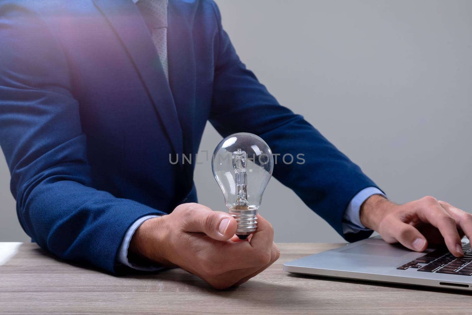 Midsection of caucasian businessman holding light bulb using laptop, isolated on grey background by Wavebreakmedia