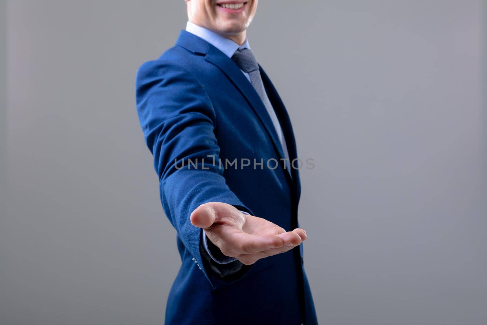 Smiling caucasian businessman reaching his hand, isolated on grey background by Wavebreakmedia