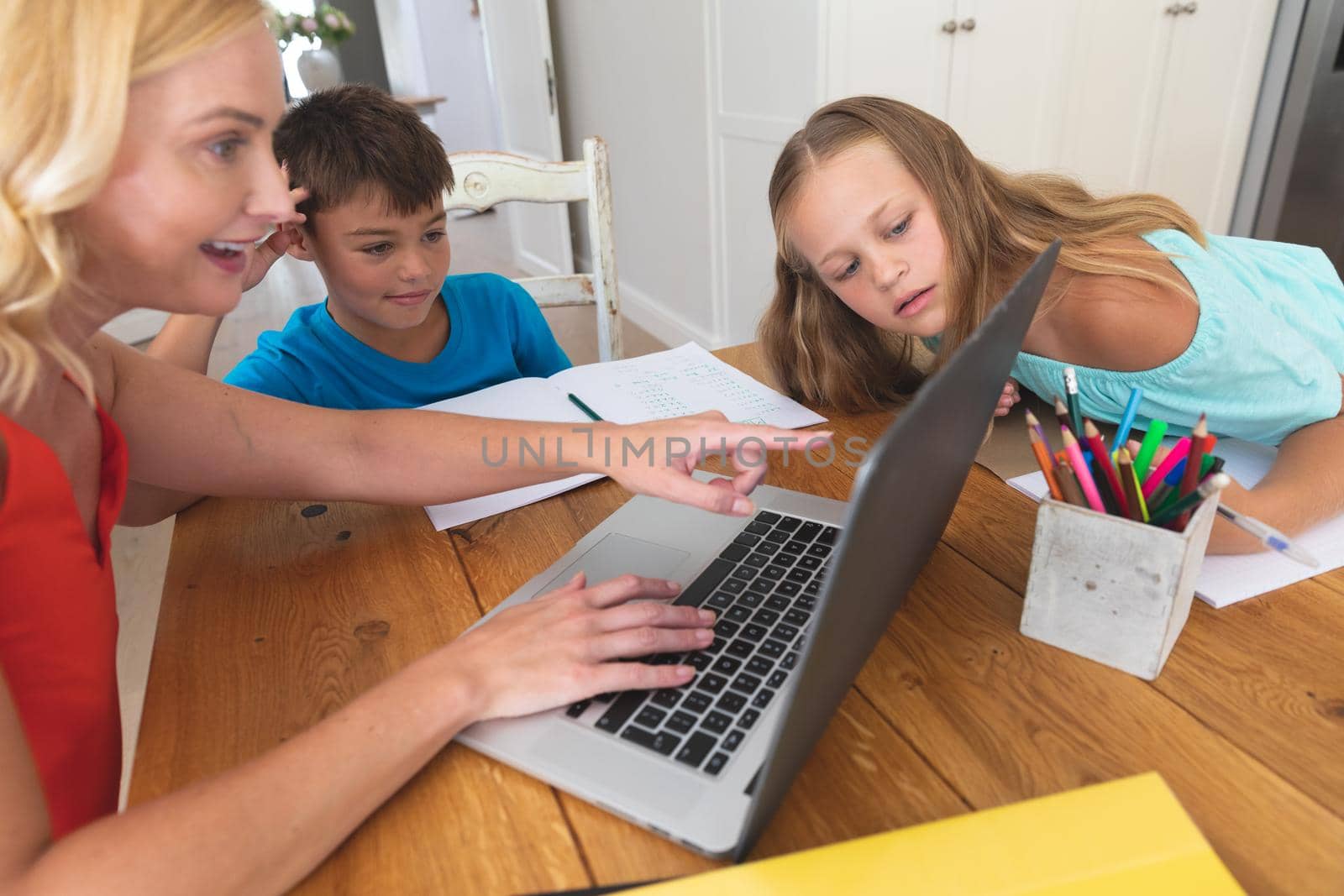 Caucasian mother using laptop and doing homework with her daughter and son smiling at home. family domestic life, spending time learning together at home.