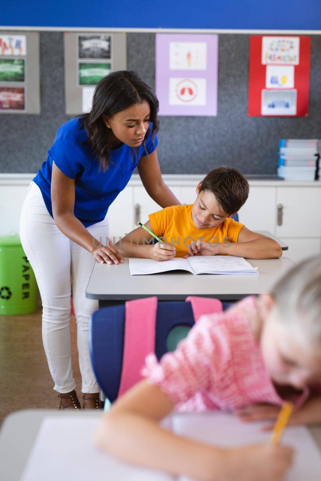 African american female teacher teaching caucasian boy in the class at elementary school. school and education concept