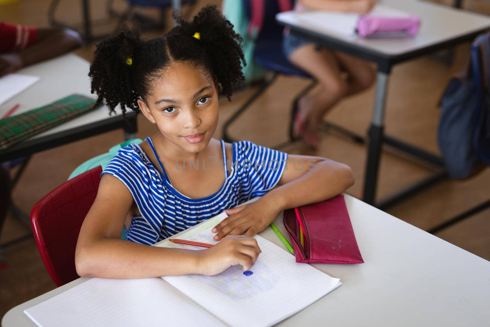 Portrait of african american girl smiling while sitting in the class at elementary school. school and education concept