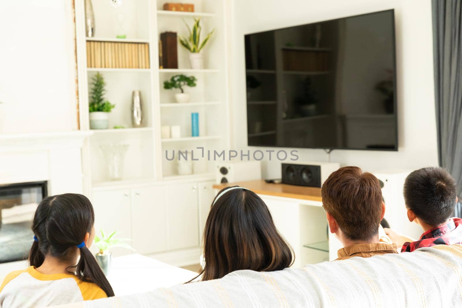 Asian couple with son and daughter sitting on couch watching television at home. domestic lifestyle and leisure family time concept.