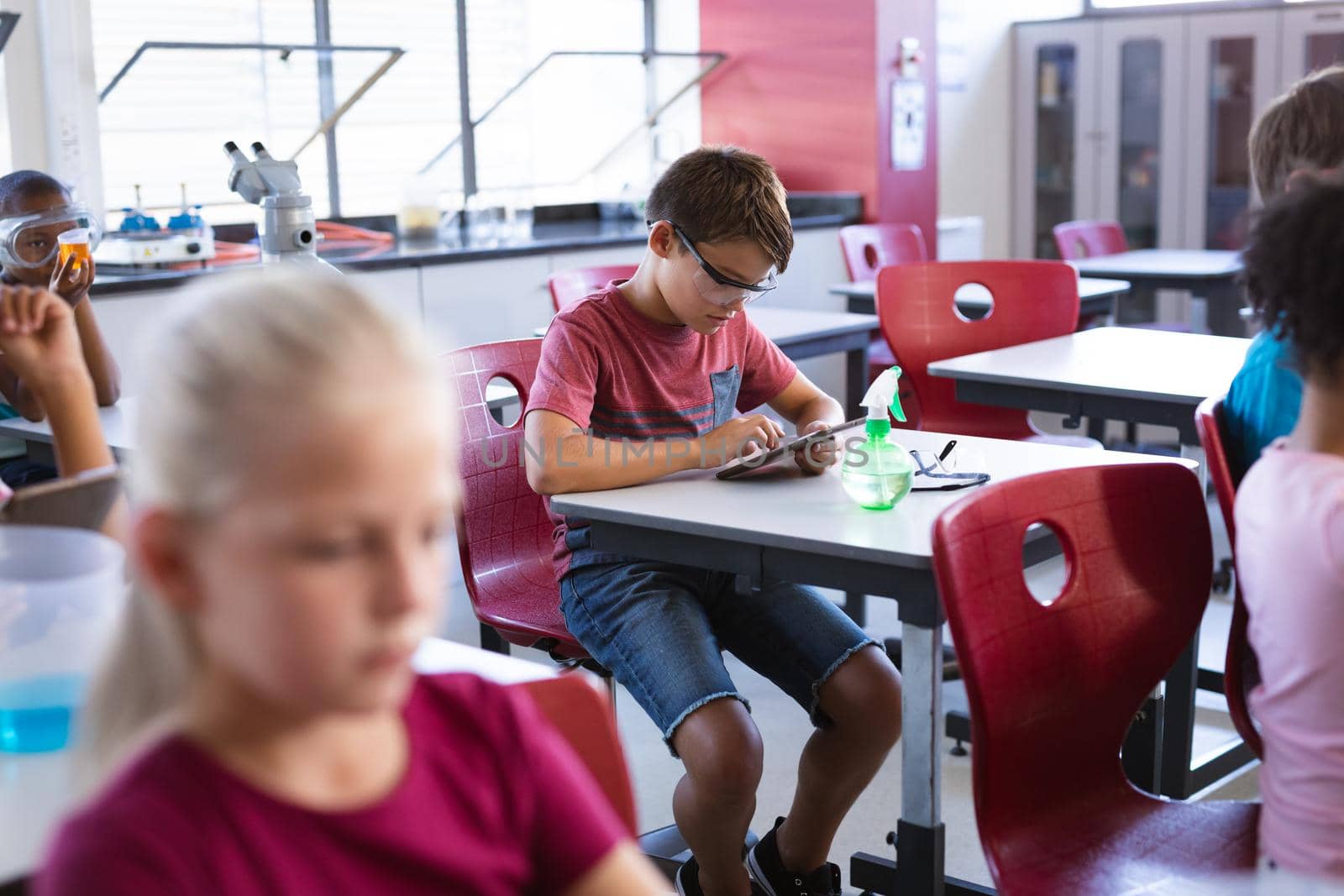 Caucasian boy wearing protective glasses using digital tablet in science class at laboratory. school and education concept