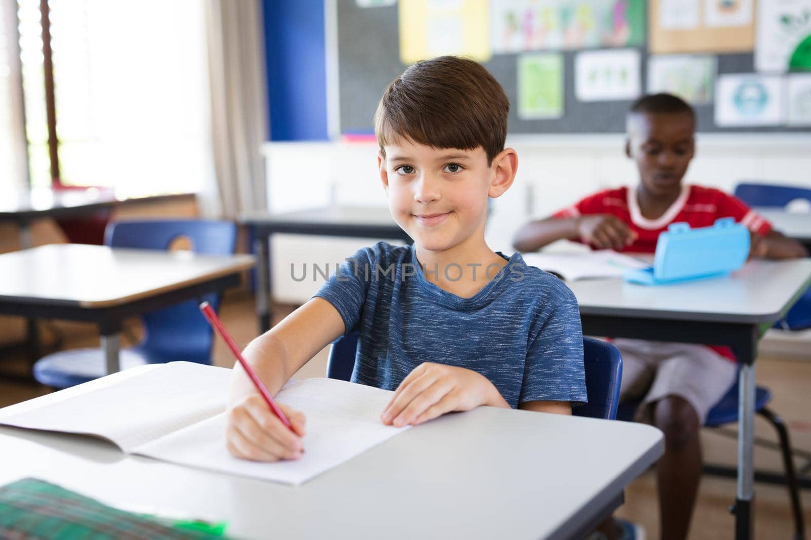 Portrait of caucasian boy smiling while sitting on his desk in the class at school by Wavebreakmedia