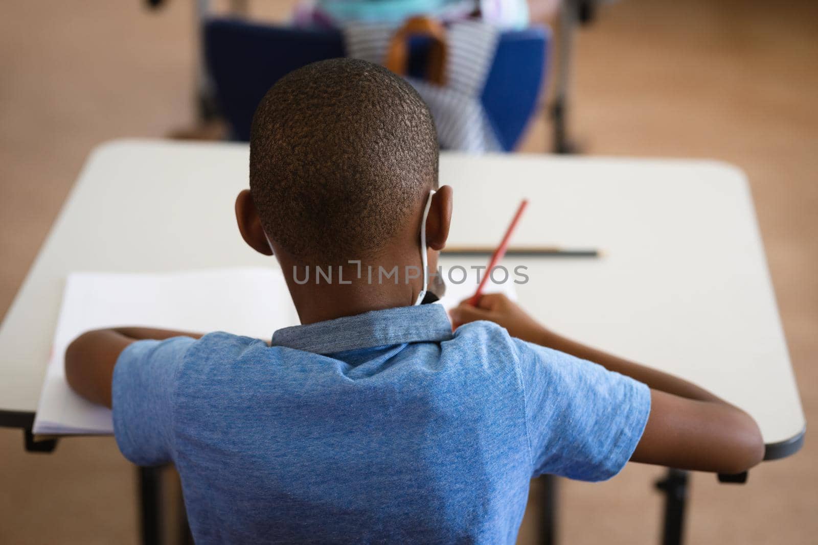 Rear view of african american boy studying while sitting on his desk in the class at school. education back to school health safety during covid19 coronavirus pandemic