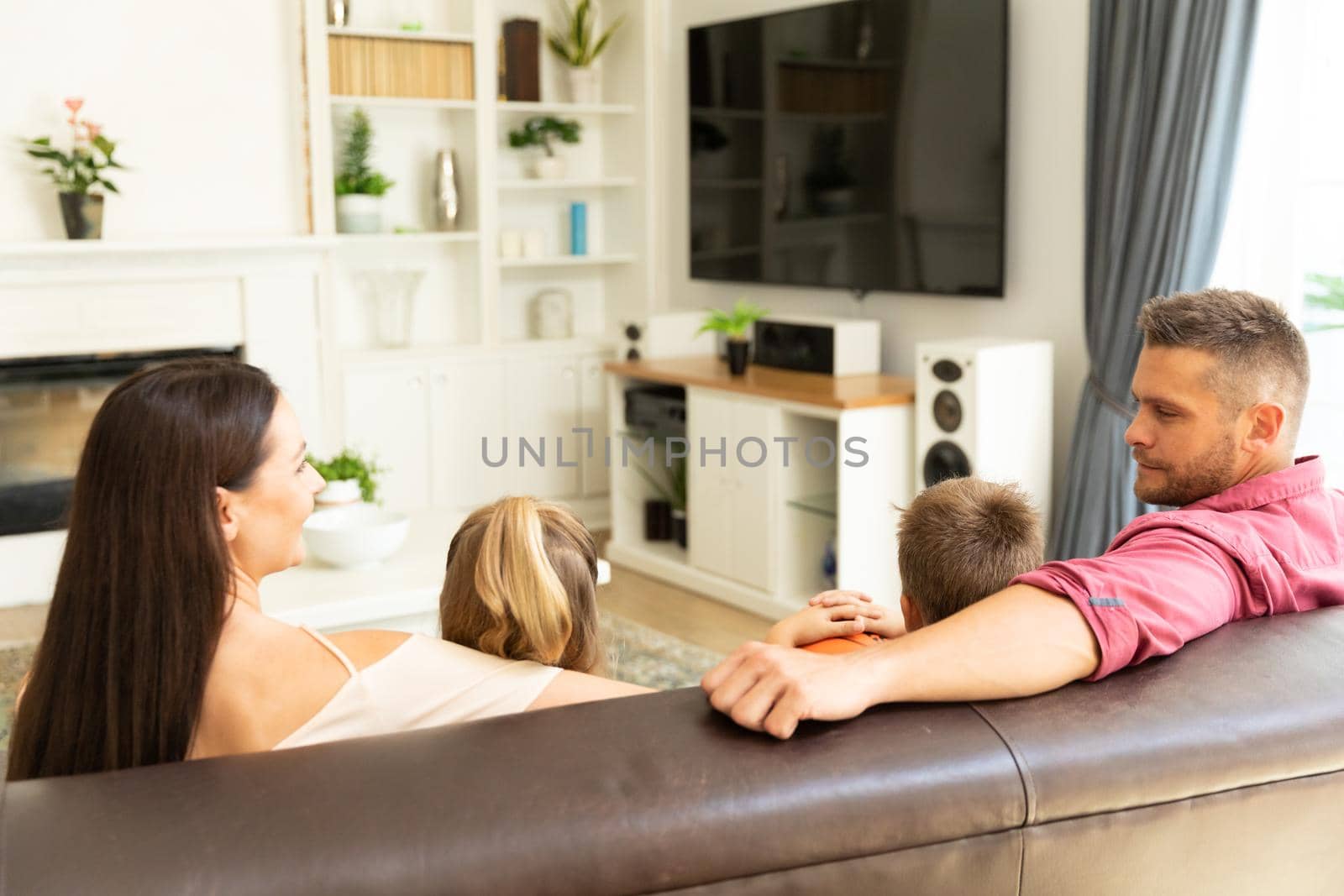 Caucasian couple with son and daughter sitting on couch watching television at home. domestic lifestyle and leisure family time concept.