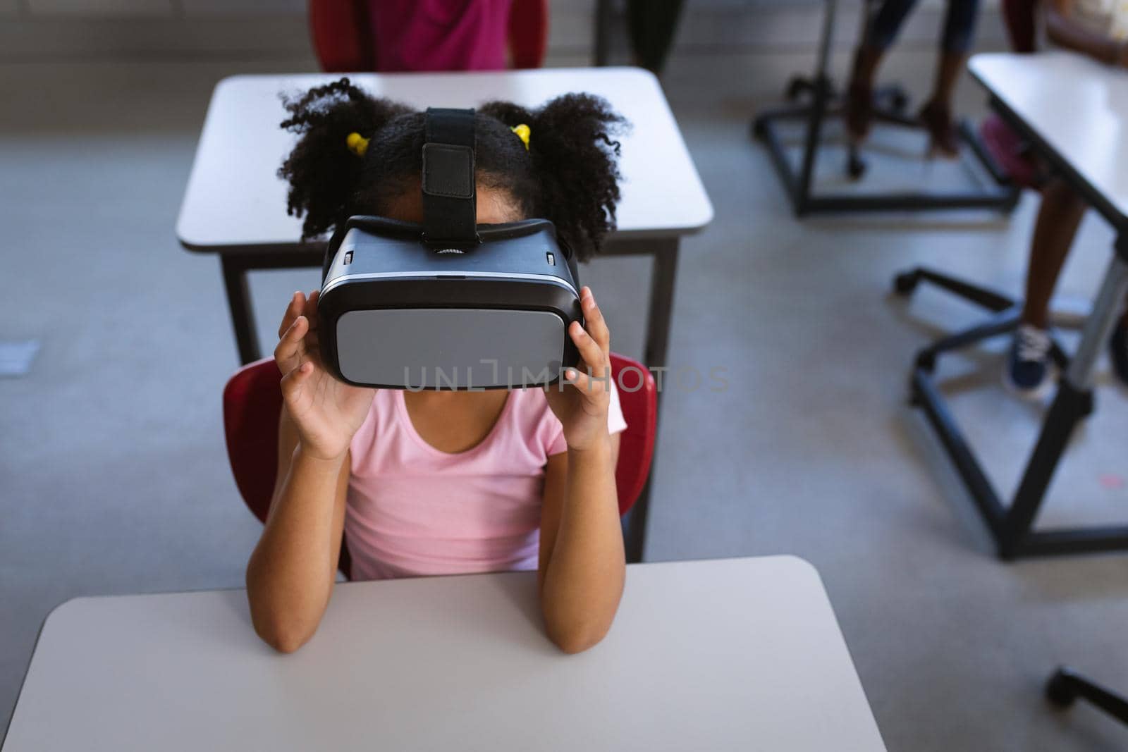 African american girl wearing vr headset while sitting on her desk in class at school. school and education concept