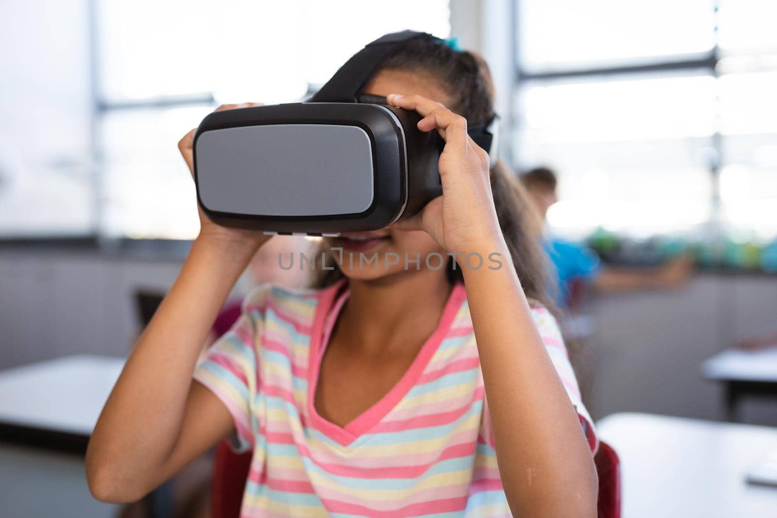 African american girl wearing vr headset while sitting on her desk in the class at school. school and education concept