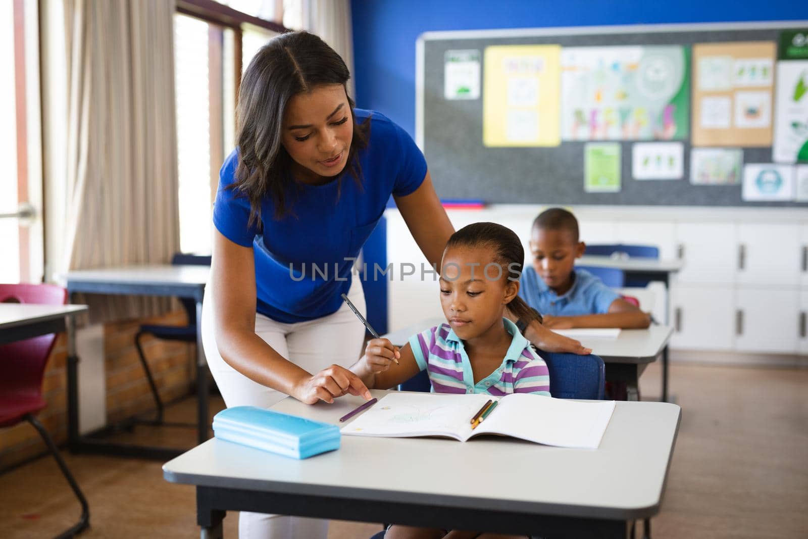 African american female teacher teaching african american girl in the class at elementary school. school and education concept