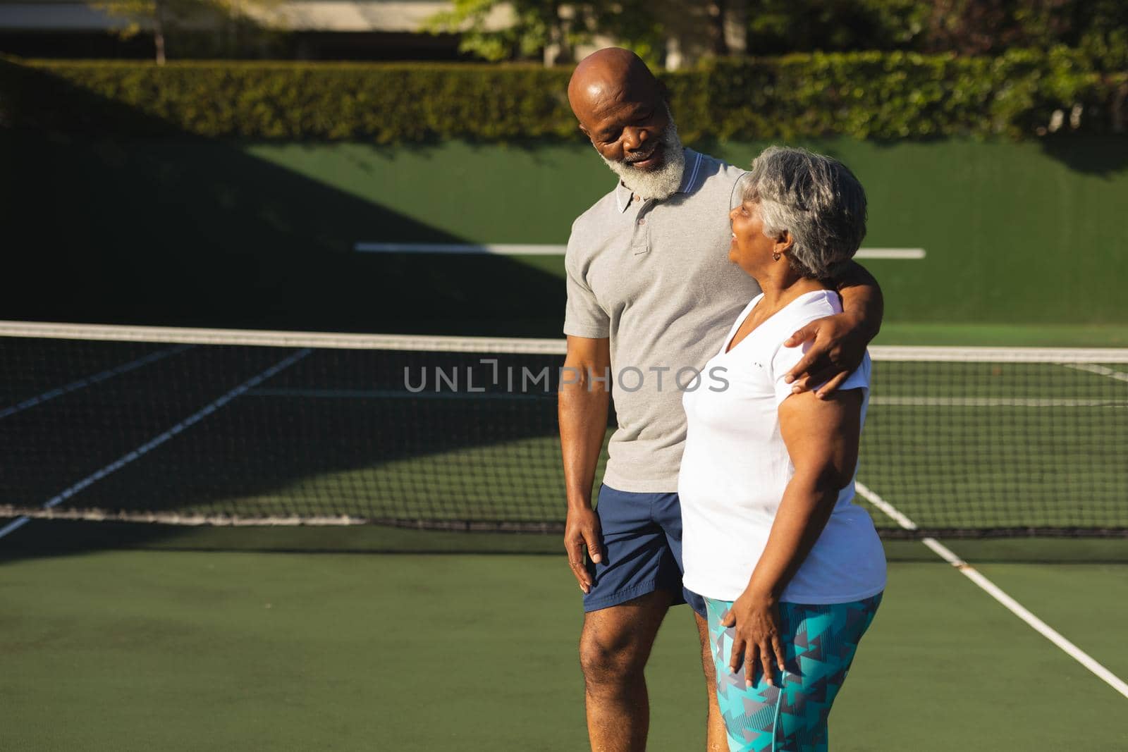 Portrait of smiling senior african american couple embracing on tennis court. retirement and active senior lifestyle concept.