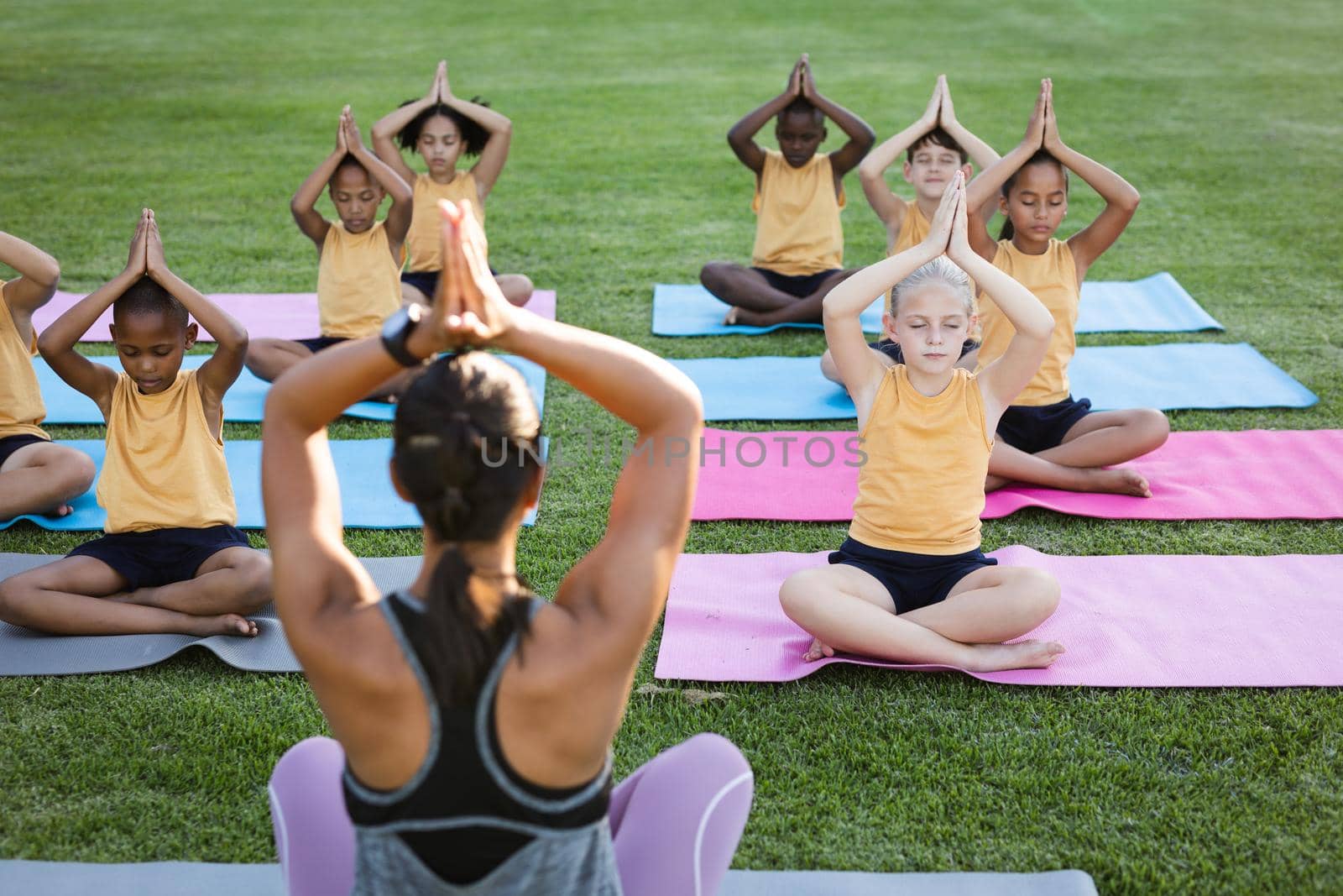 Female teacher and group of diverse students practicing yoga and meditating in the garden at school. school and education concept