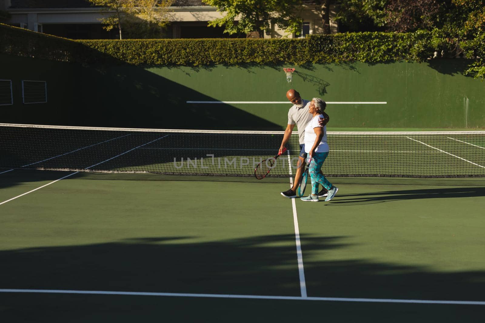 Portrait of smiling senior african american couple with tennis rackets on tennis court. retirement and active senior lifestyle concept.