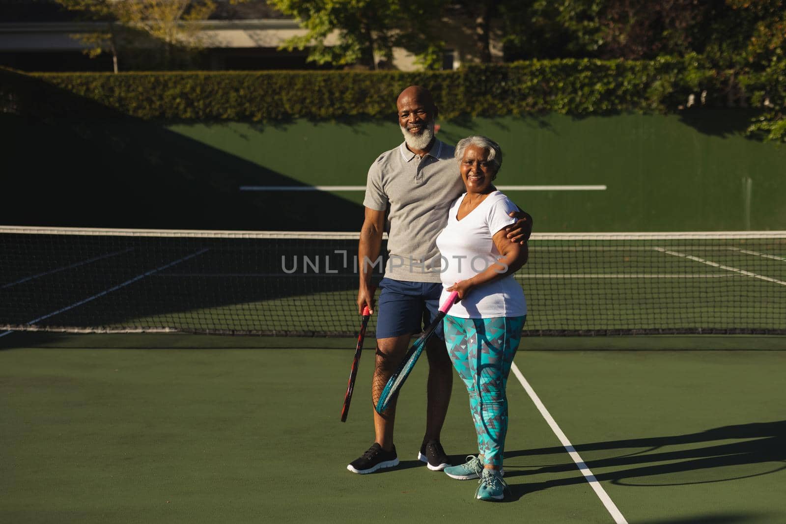 Portrait of smiling senior african american couple with tennis rackets on tennis court. retirement and active senior lifestyle concept.