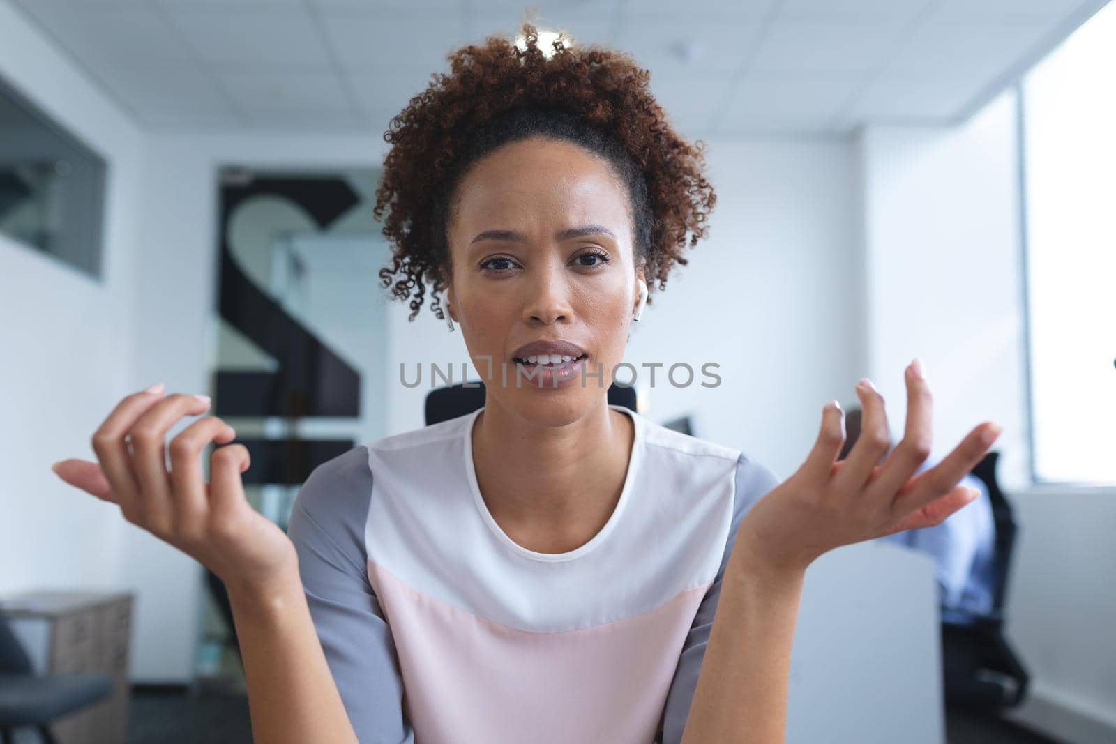 Portrait of mixed race businesswoman sitting at desk with colleague in background by Wavebreakmedia