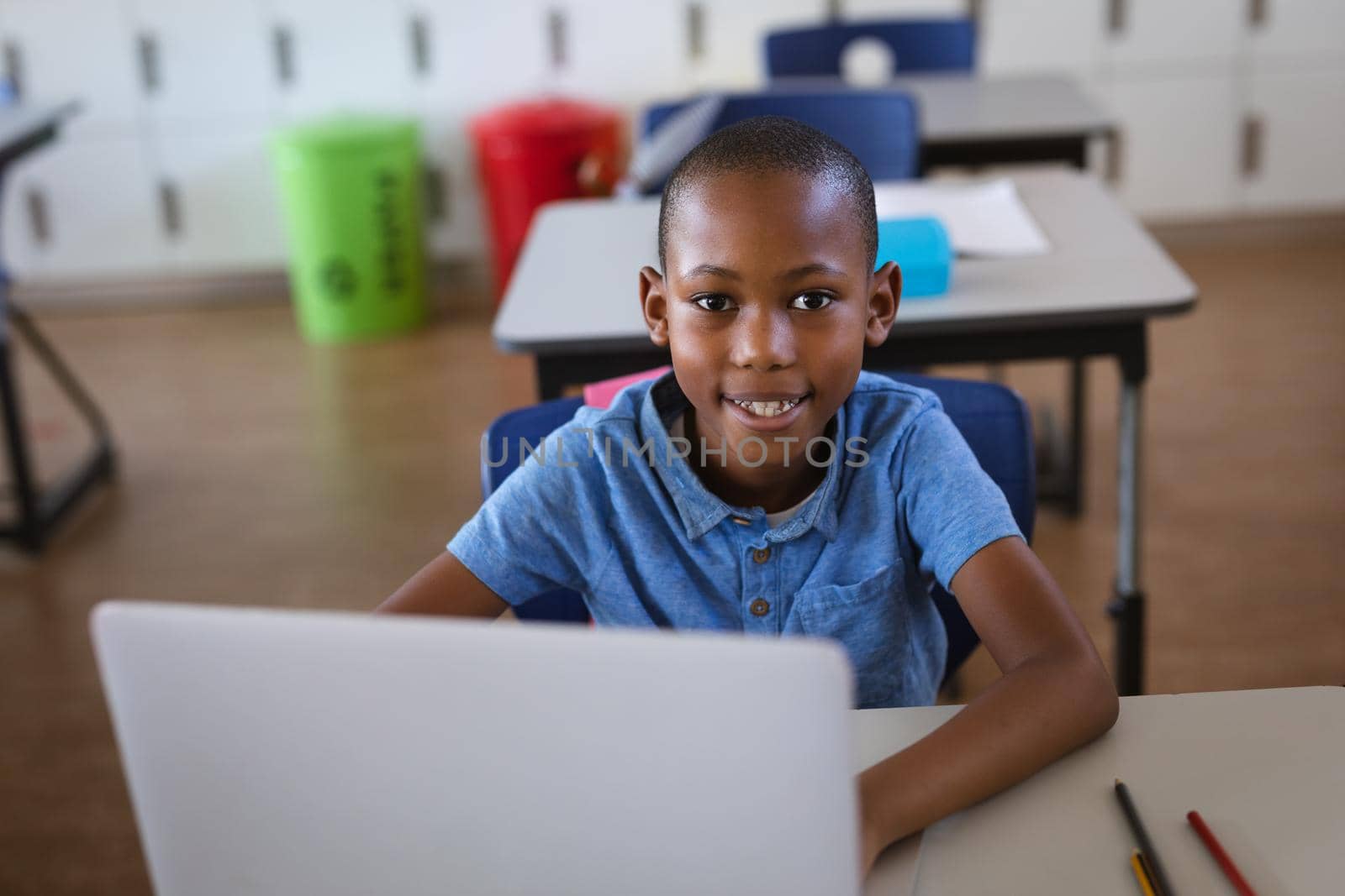 Portrait of african american boy smiling while using laptop sitting on his desk at elementary school by Wavebreakmedia