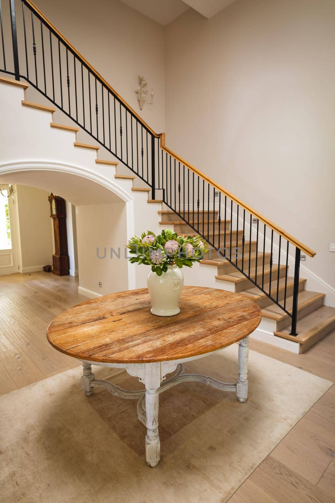 General view of house interior with table and vase with flowers in spacious hallway and staircase by Wavebreakmedia