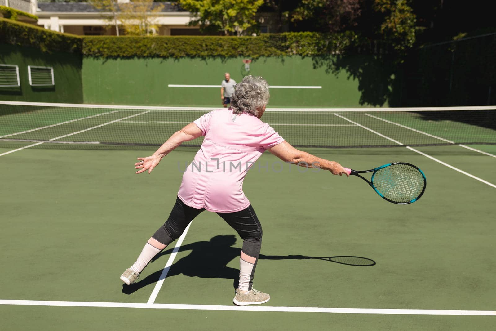 Senior caucasian couple playing tennis together on court. retirement retreat and active senior lifestyle concept.