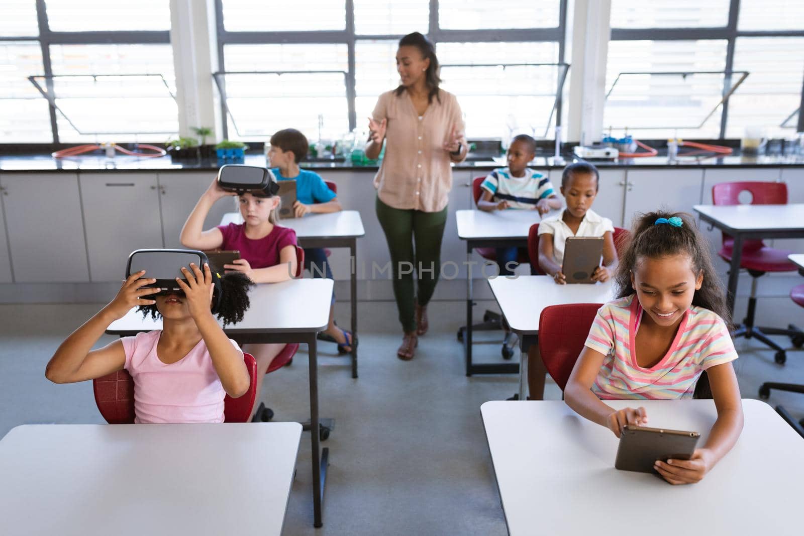 African american female teacher teaching students to use electronic devices in the class at school. school and education concept