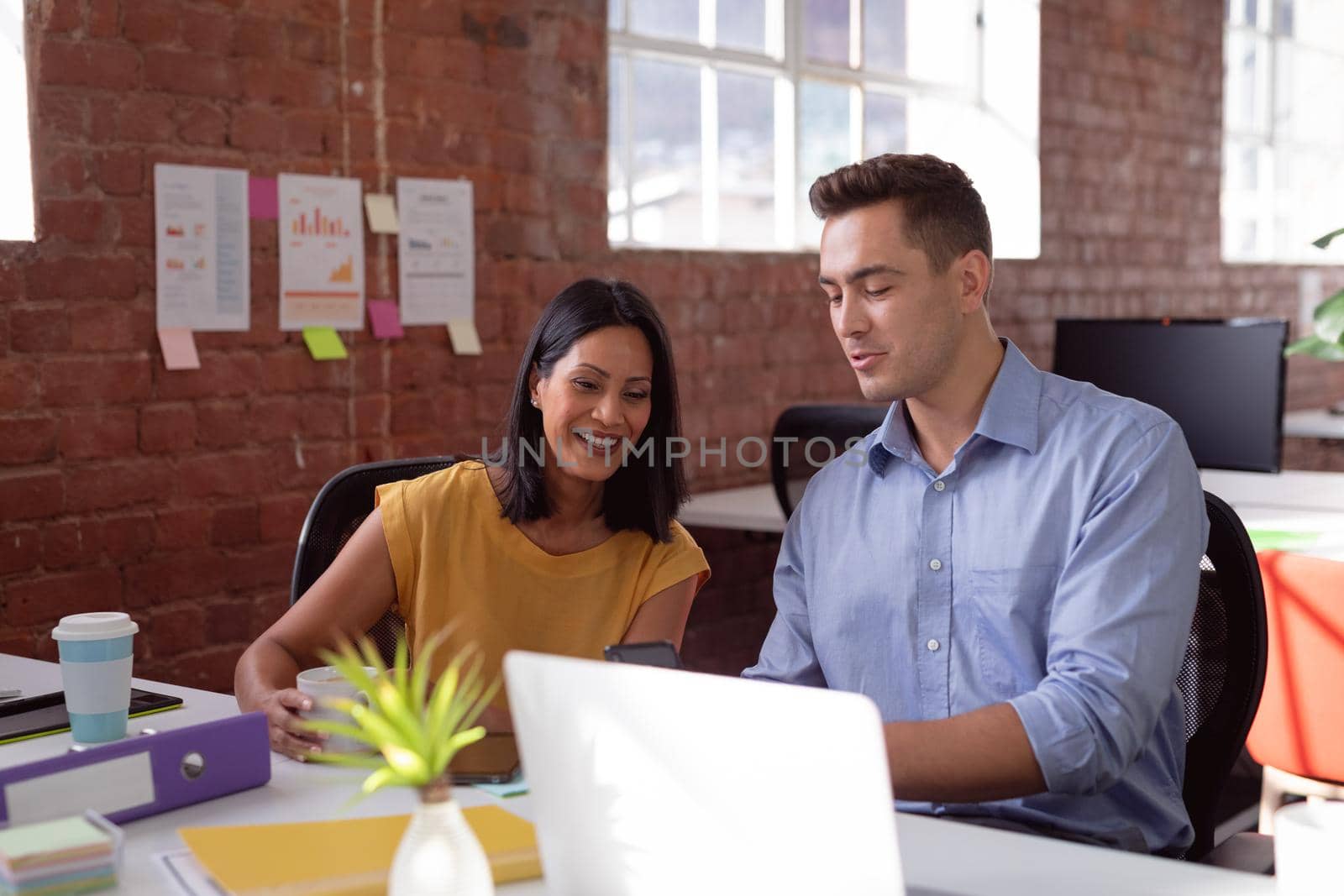 Happy caucasian male and female colleague sitting at desk talking and smiling. working in business at a modern office.