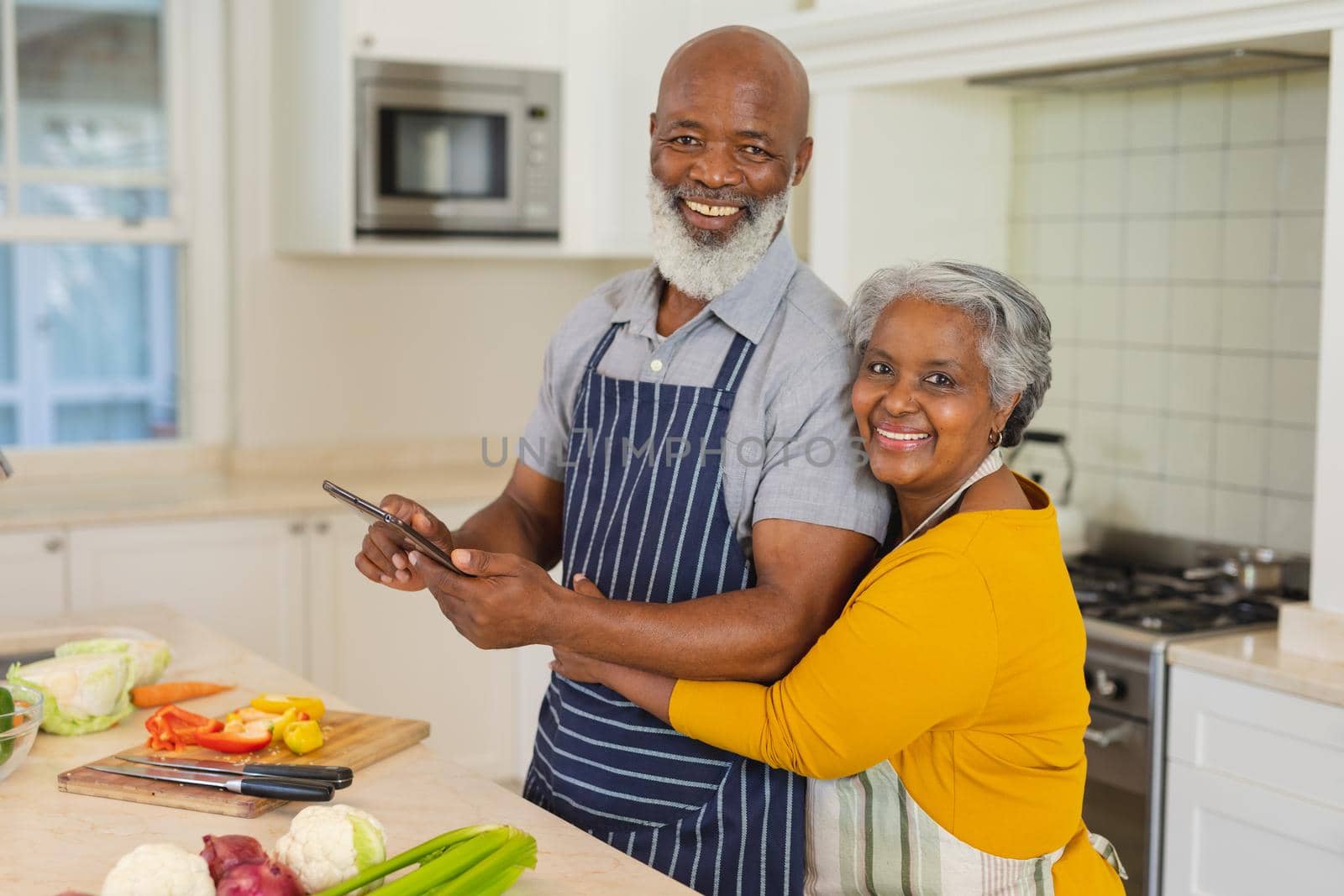Portrait of senior african american couple cooking together in kitchen using tablet. retreat, retirement and happy senior lifestyle concept.