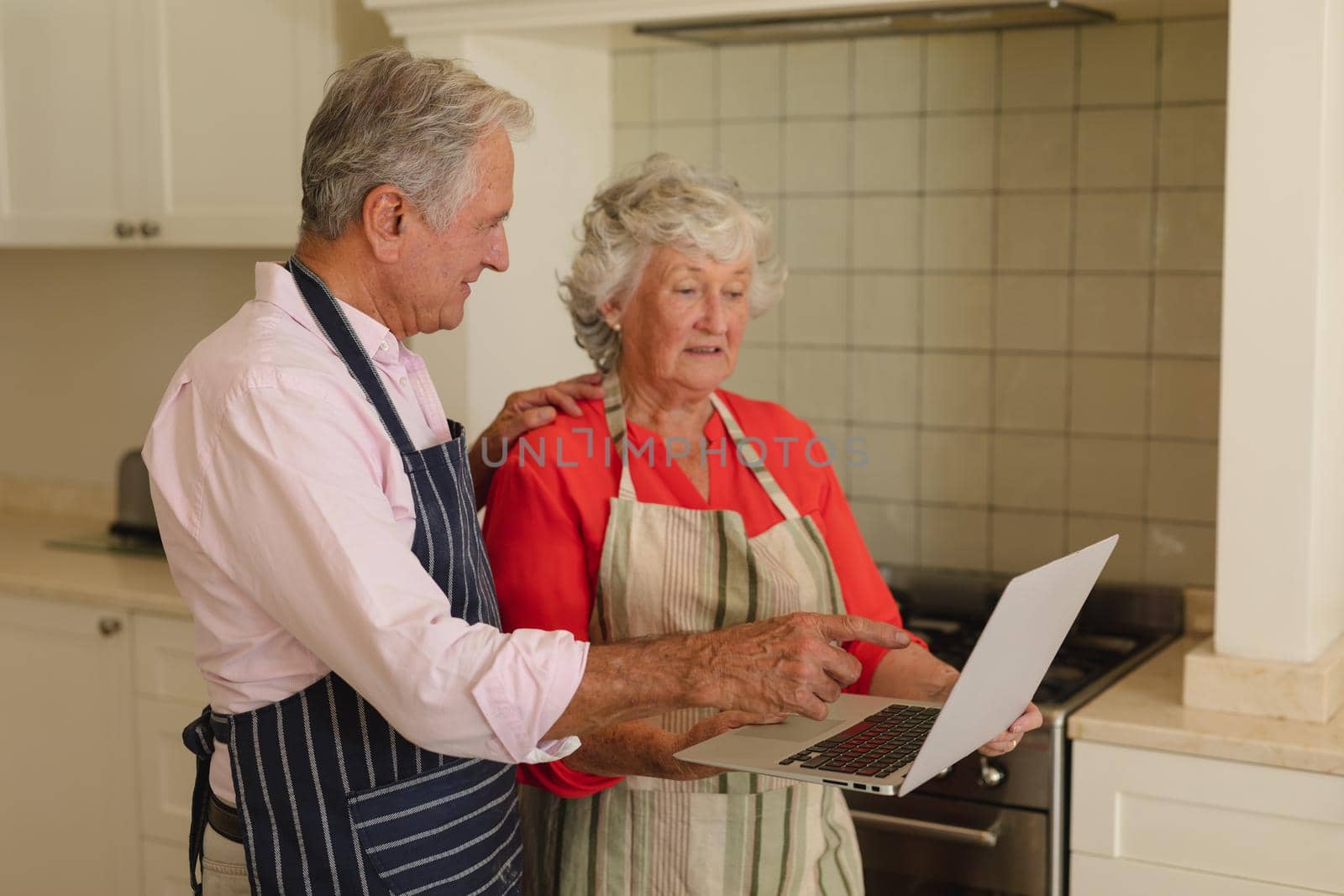 Senior caucasian couple using laptop together in kitchen. retreat, retirement and happy senior lifestyle concept.