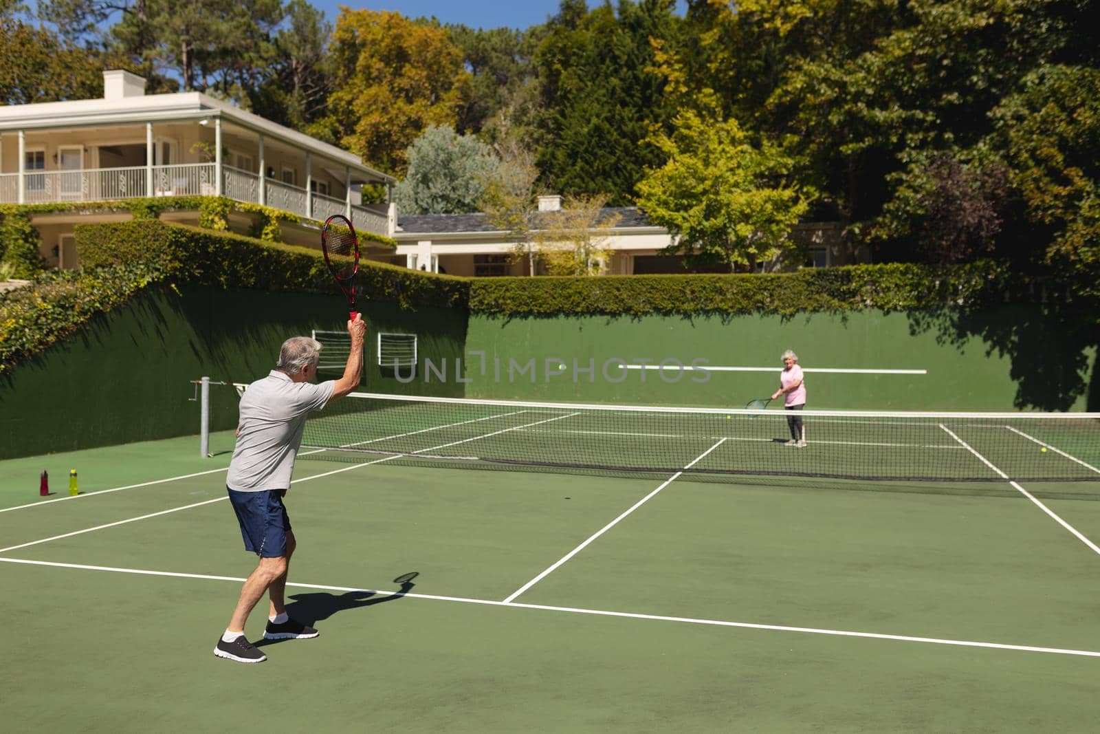 Senior caucasian couple playing tennis together on court. retirement retreat and active senior lifestyle concept.