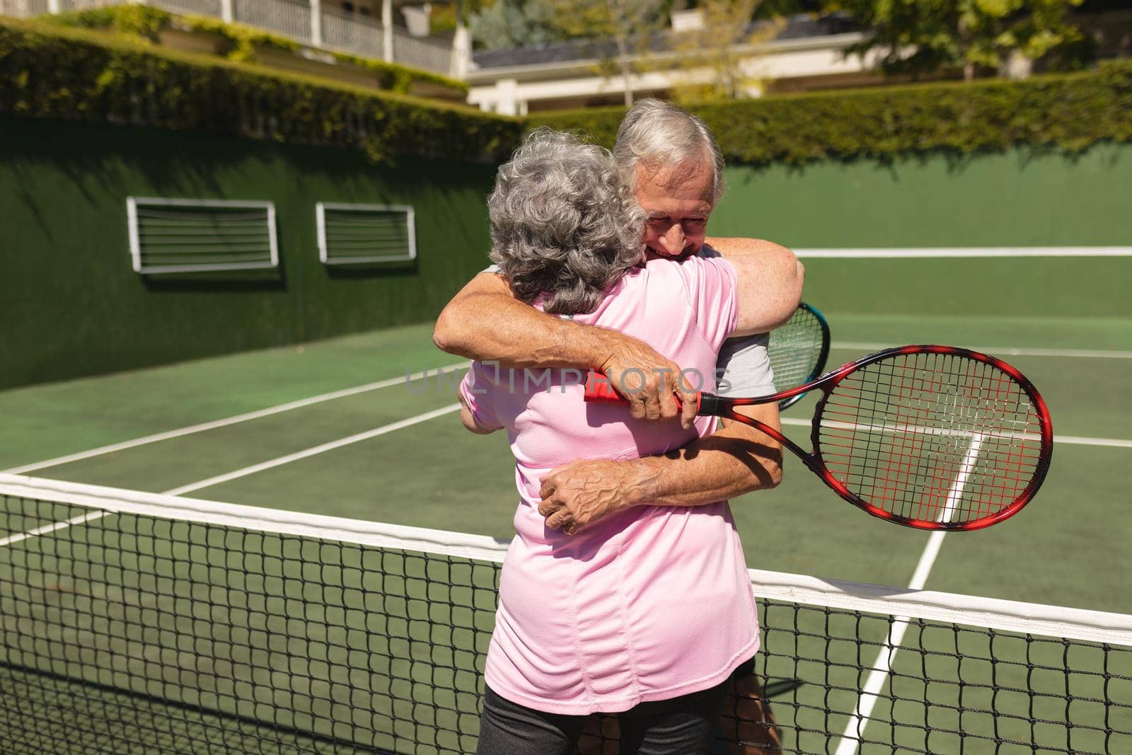 Senior caucasian couple playing tennis together on court embracing. retirement retreat and active senior lifestyle concept.