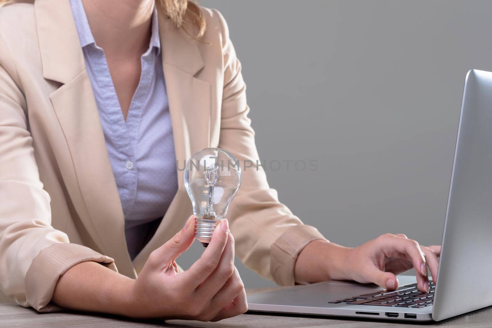 Midsection of caucasian businesswoman holding light bulb using laptop, isolated on grey background by Wavebreakmedia