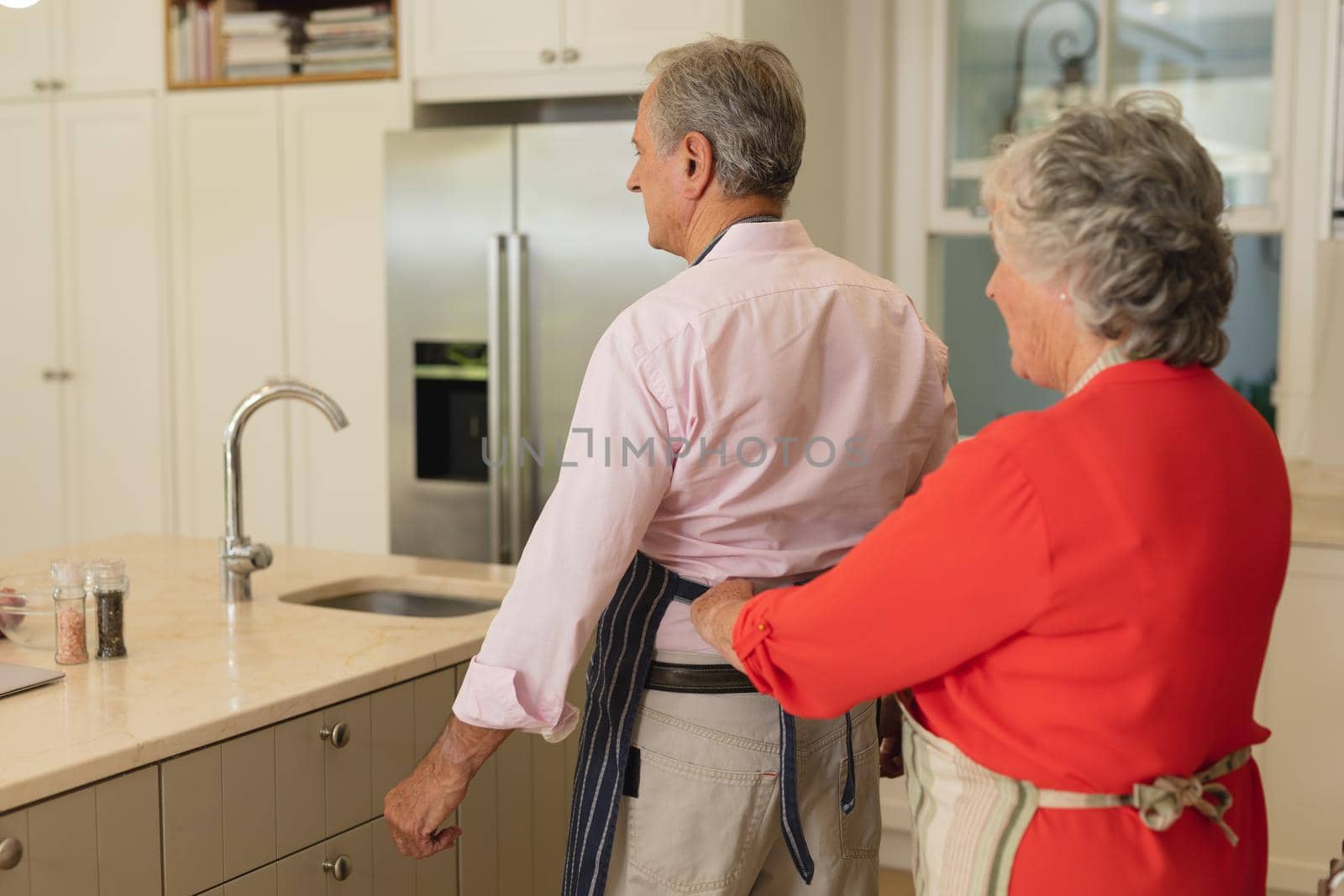 Senior caucasian couple tying apron and smiling in kitchen by Wavebreakmedia