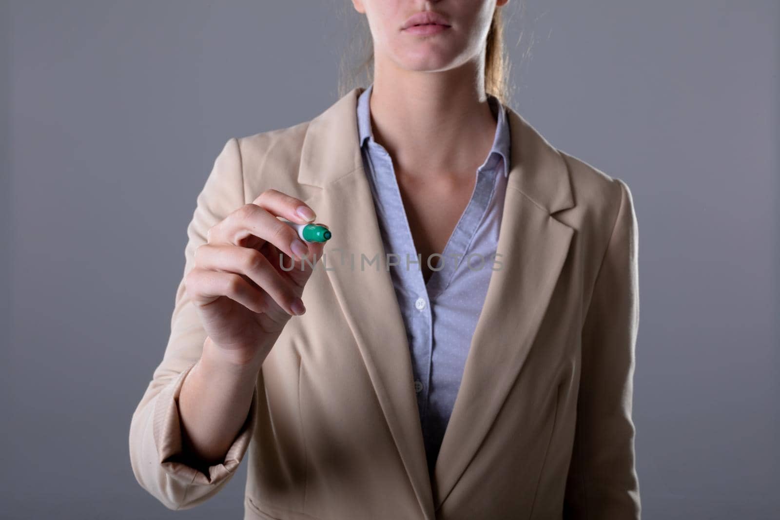 Caucasian businesswoman holding green marker, isolated on grey background by Wavebreakmedia