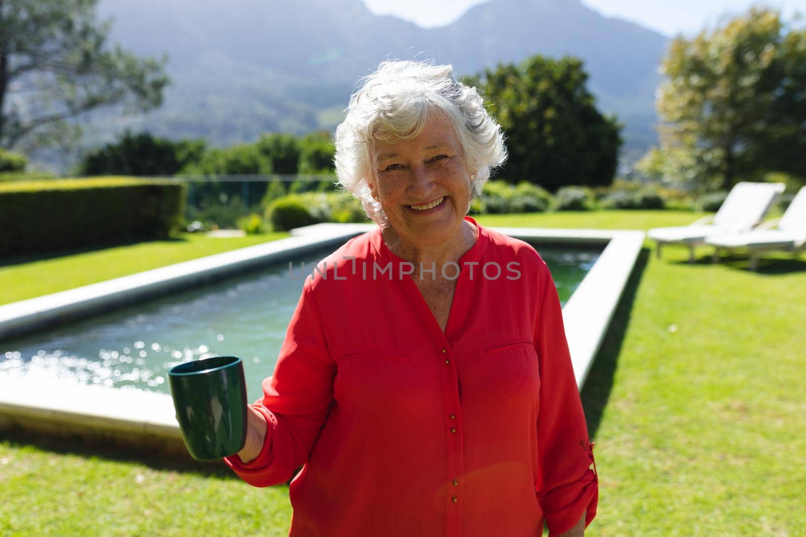 Portrait of senior caucasian woman smiling and holding mug in sunny garden. retreat, retirement and happy senior lifestyle concept.