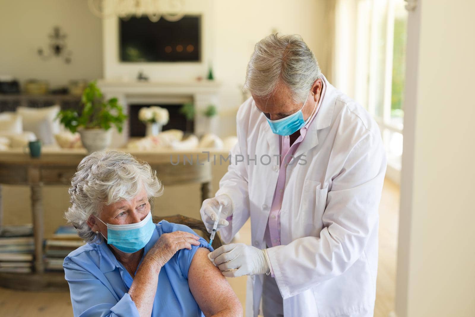 Senior caucasian male doctor vaccinating female patient wearing face masks. medicine and healthcare services during covid 19 pandemic concept.