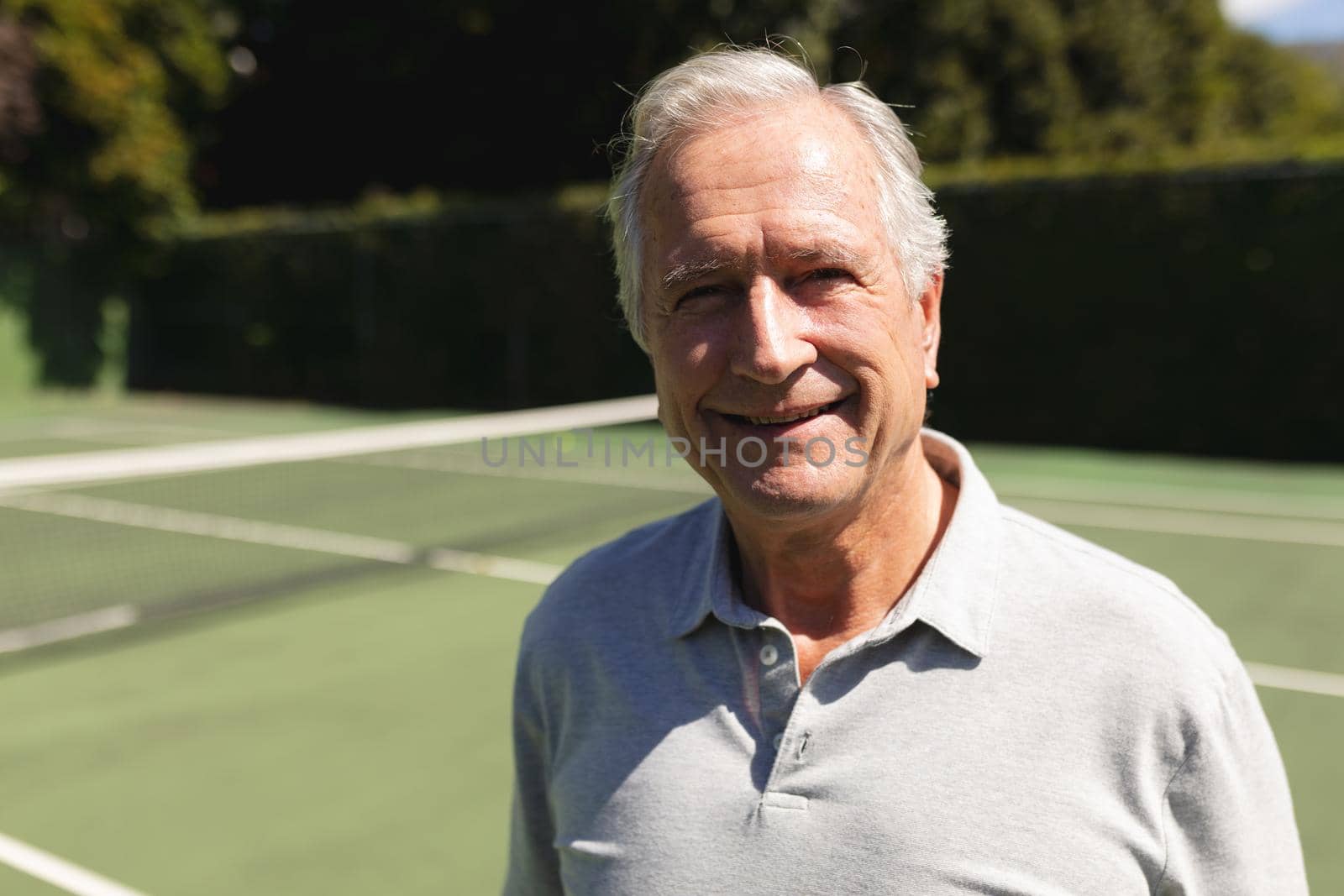 Portrait of senior caucasian man looking at camera and smiling on tennis court. retirement retreat and active senior lifestyle concept.