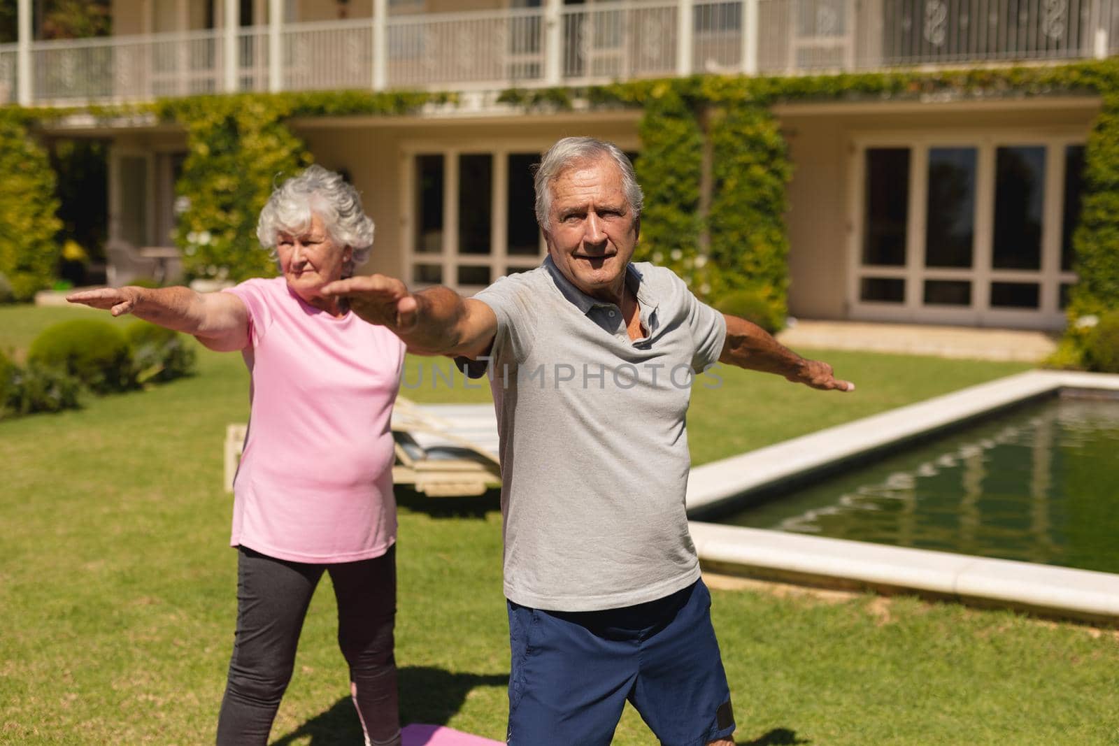 Senior caucasian couple practicing yoga, stretching in sunny garden. retirement retreat and active senior lifestyle concept.