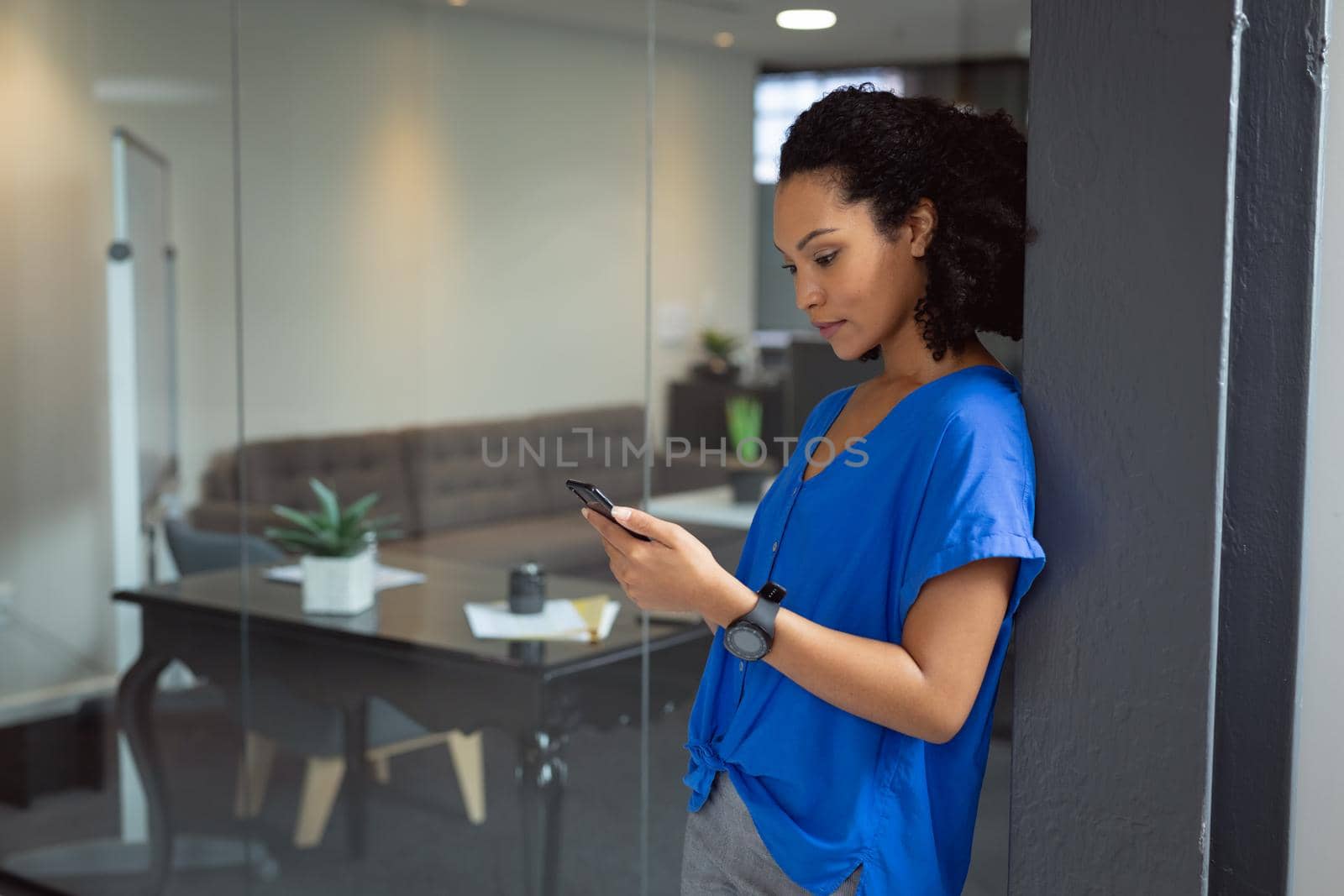 Happy african american businesswoman using smartphone leaning against door in office by Wavebreakmedia